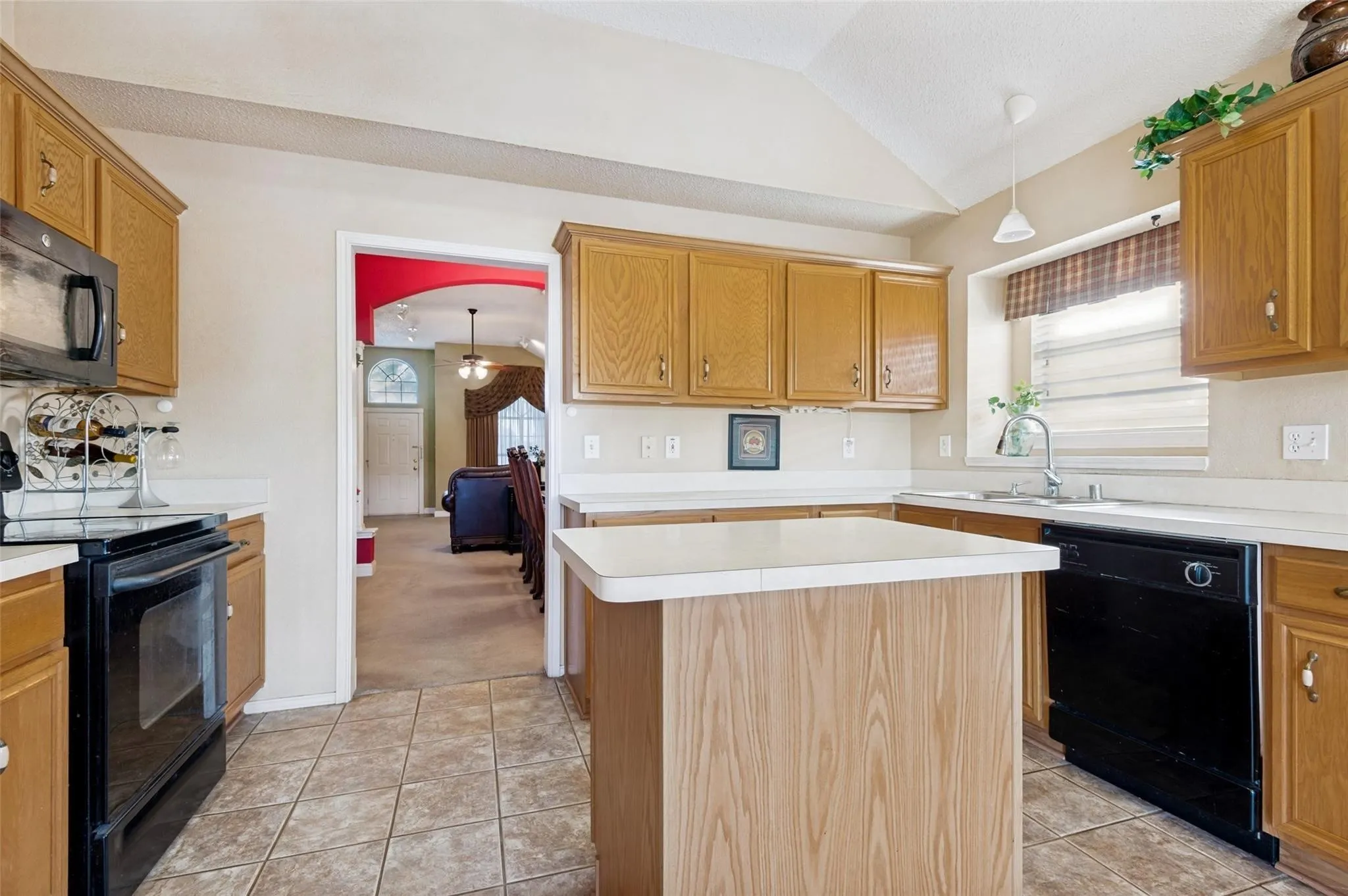 Kitchen featuring wood-finish cabinetry, white countertops, black appliances, a center island, and tile flooring