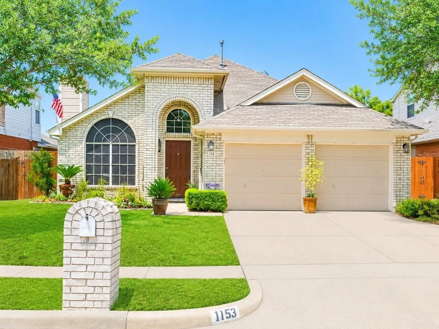 Brick exterior with arched windows, a two-car garage, and a manicured lawn