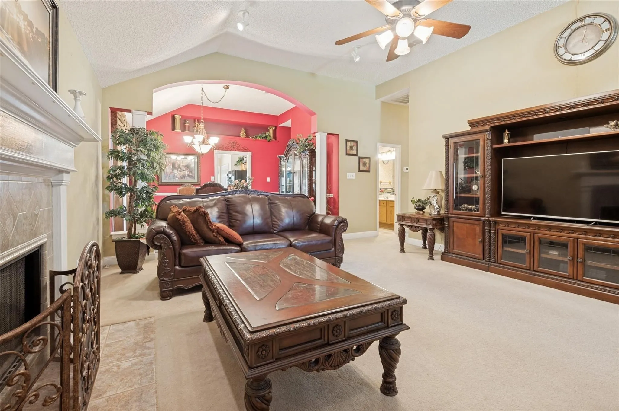 Spacious living area featuring a vaulted ceiling with a ceiling fan, a tiled fireplace with a mantel, and an arched entryway