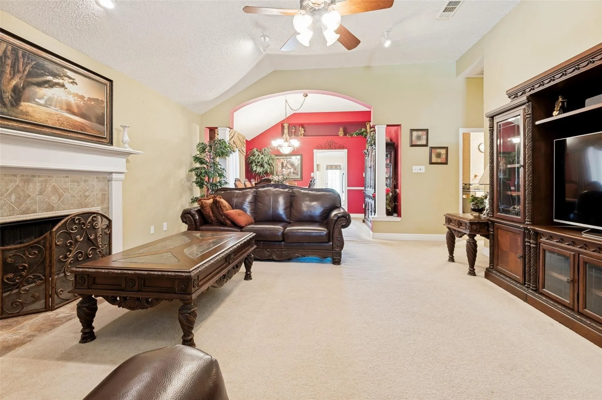 Vaulted ceiling with ceiling fan, recessed lighting, fireplace with tile surround and mantel, arched doorways, and carpet flooring