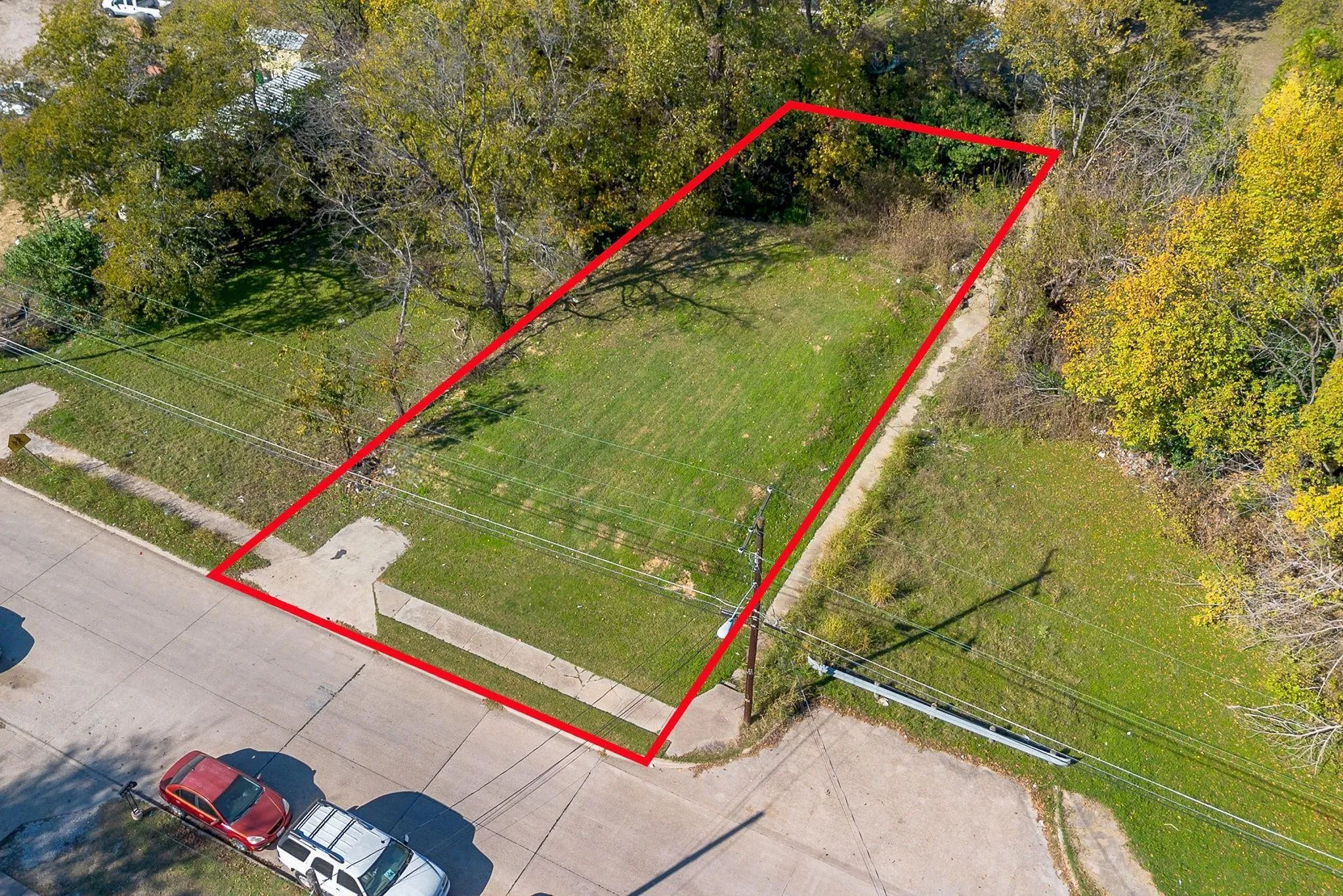 Expansive residential lot featuring a manicured lawn, mature tree line bordering the perimeter, and direct street access