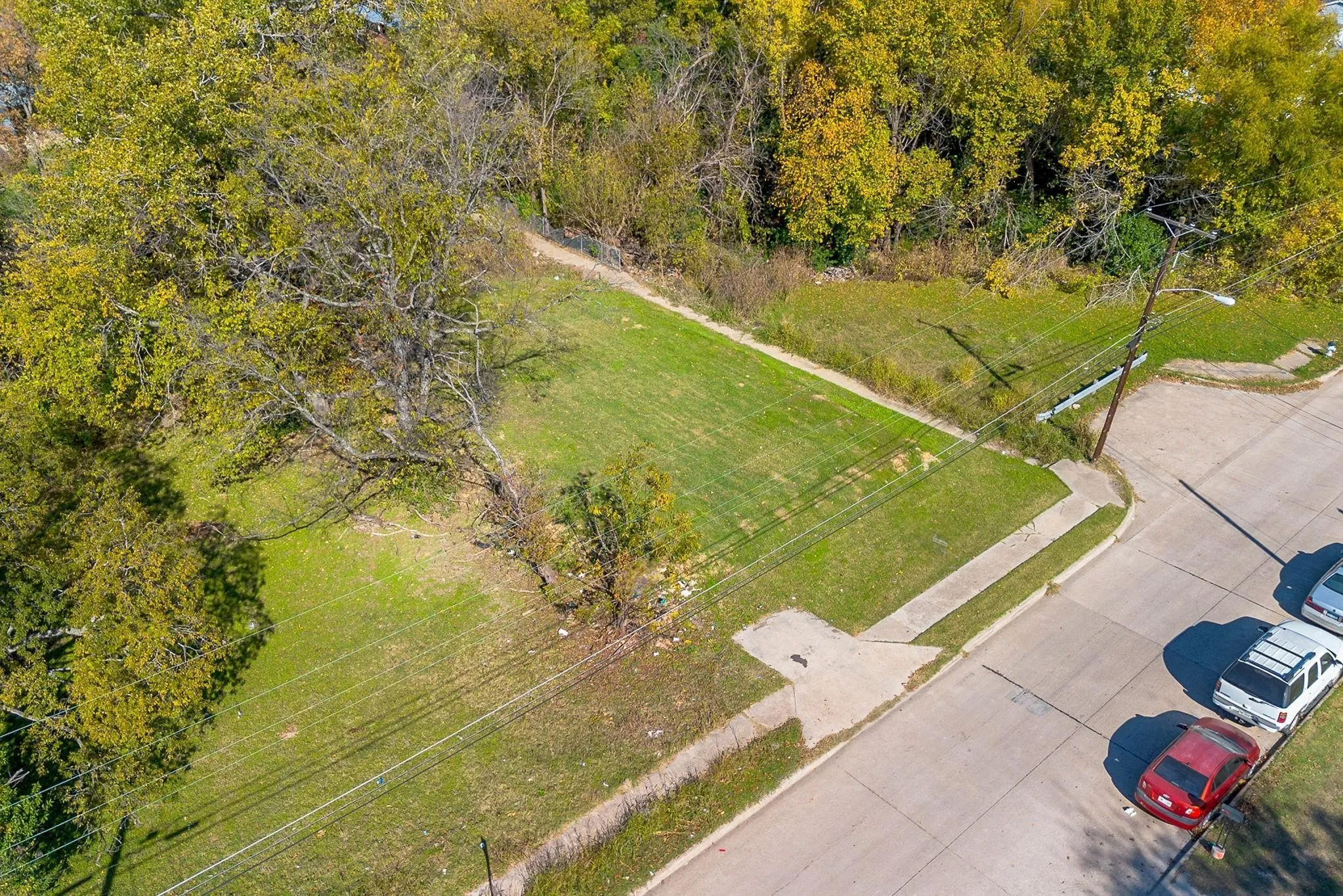 Expansive lot featuring mature trees, a manicured lawn, and paved road frontage
