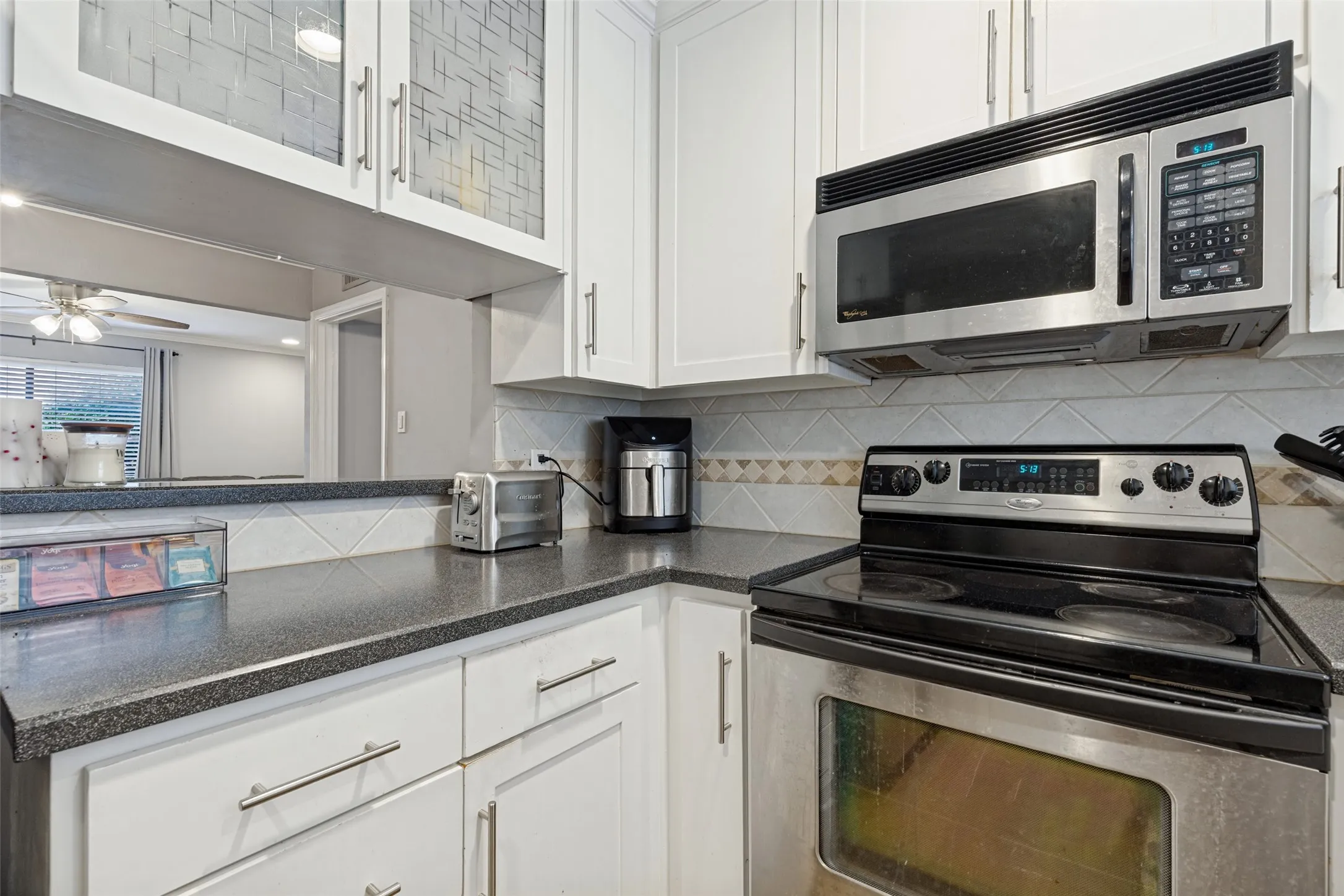 White cabinetry with stainless steel hardware, black countertop, tile backsplash, and stainless steel oven with an overhead microwave