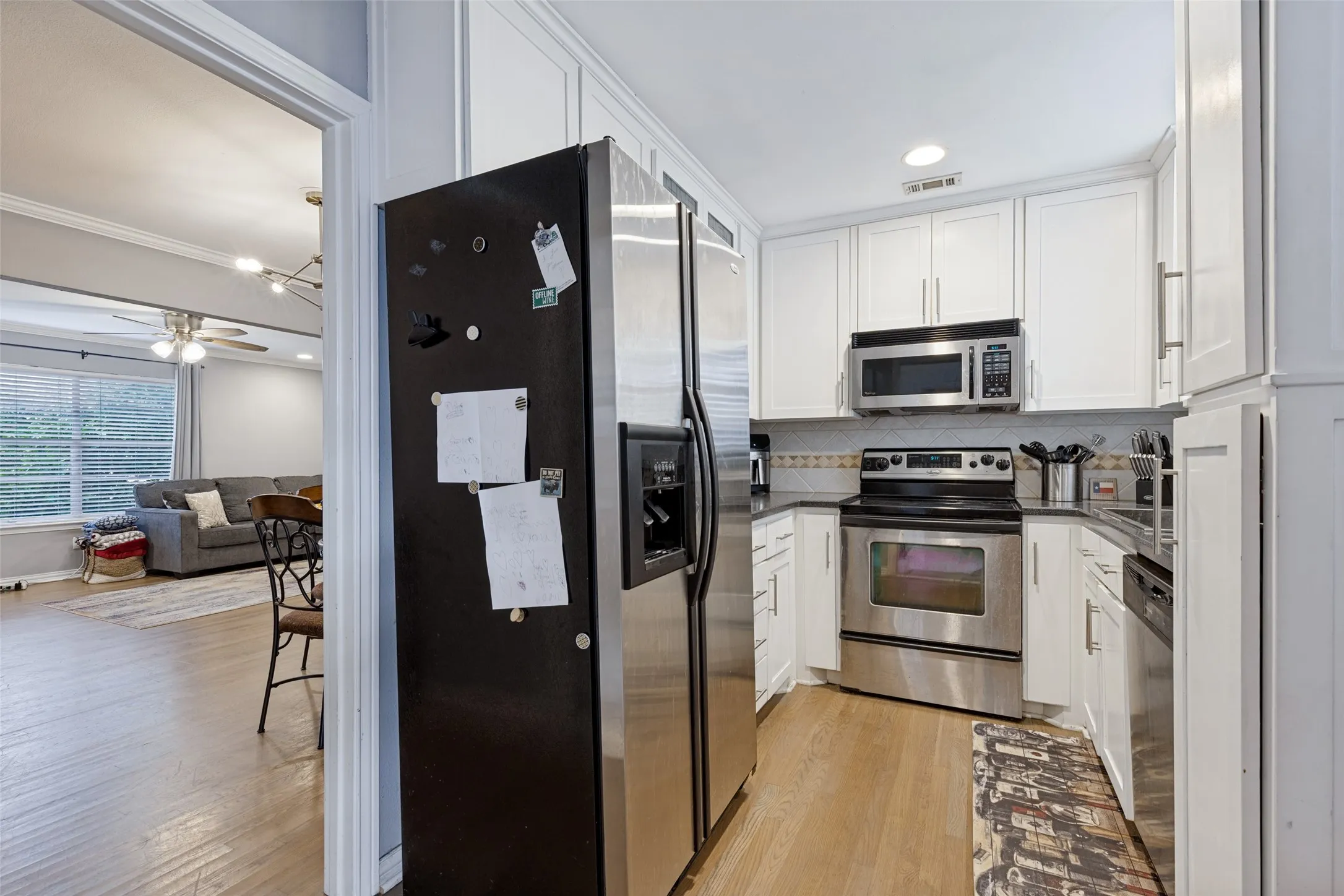 Kitchen featuring stainless steel appliances, white cabinetry, dark countertops, and wood-finish flooring