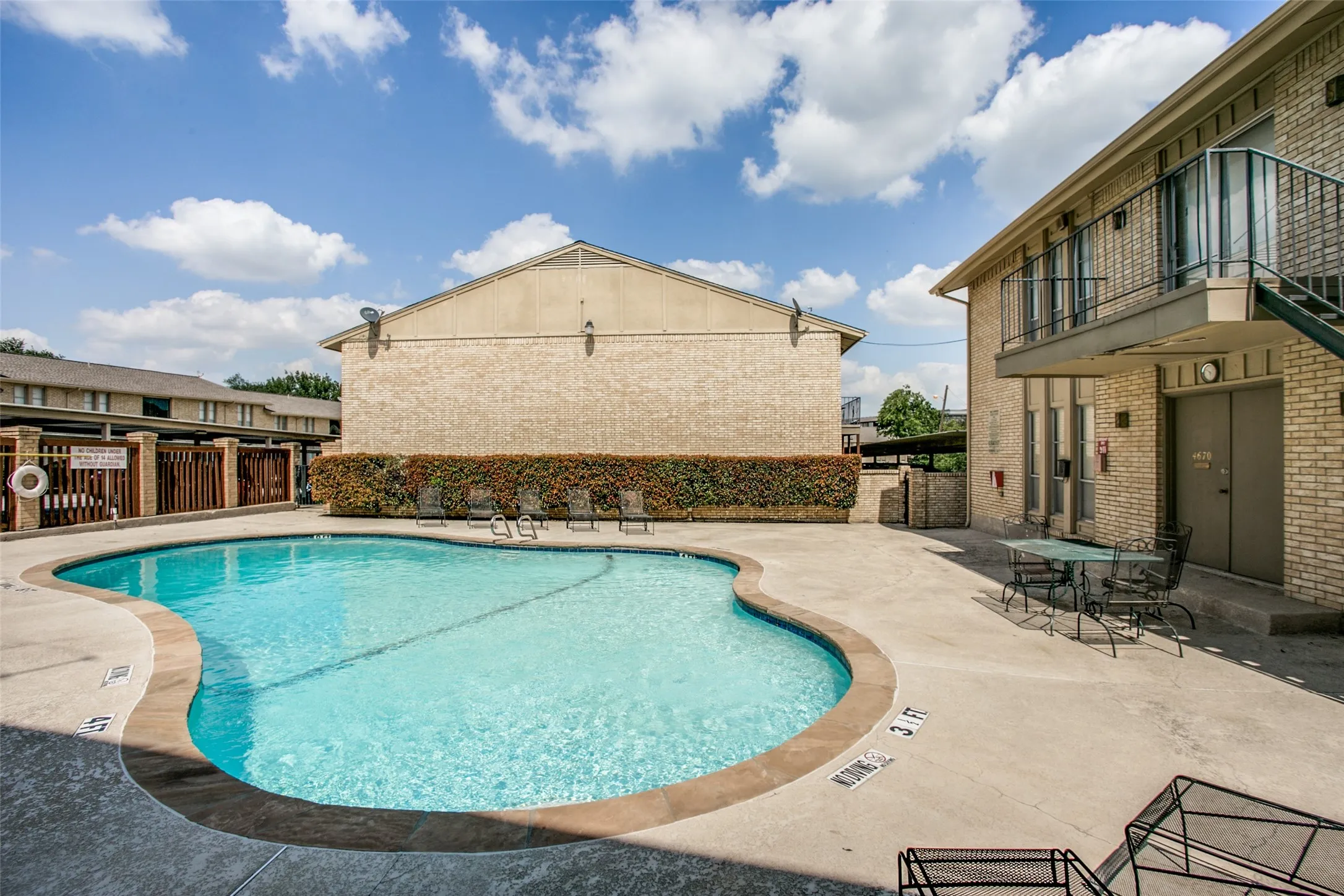 Curved swimming pool with concrete decking, surrounded by brick-clad buildings