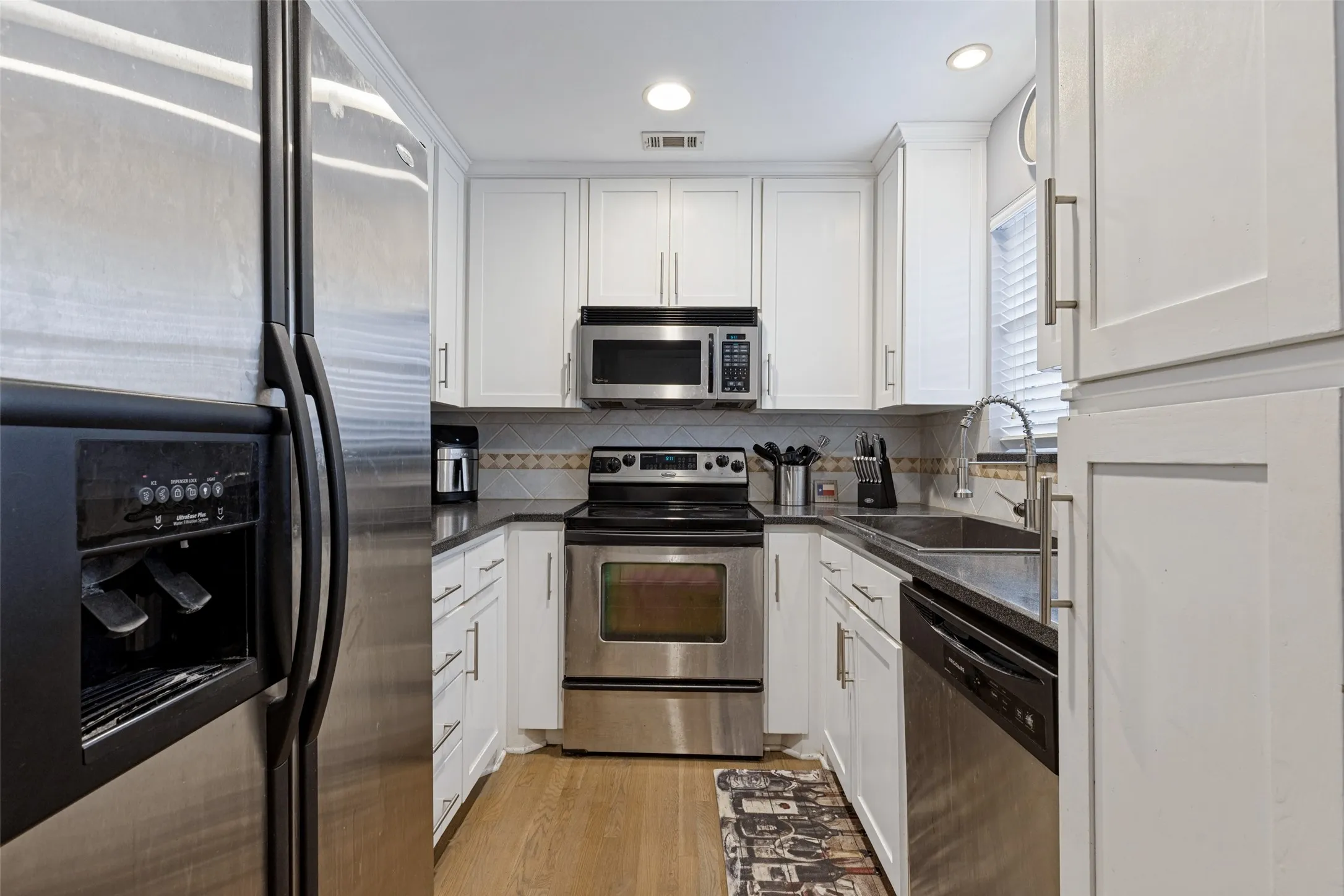 White shaker cabinetry, dark countertops, stainless steel appliances, and wood-finish flooring