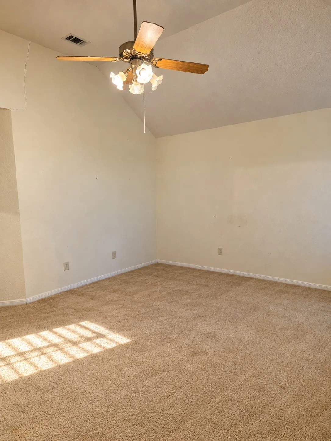 Vaulted ceiling with a brass-finish ceiling fan and integrated lighting, light-toned wall paint, and wall-to-wall carpeting.  VIRTUALLY DECLUTTERED USING AI