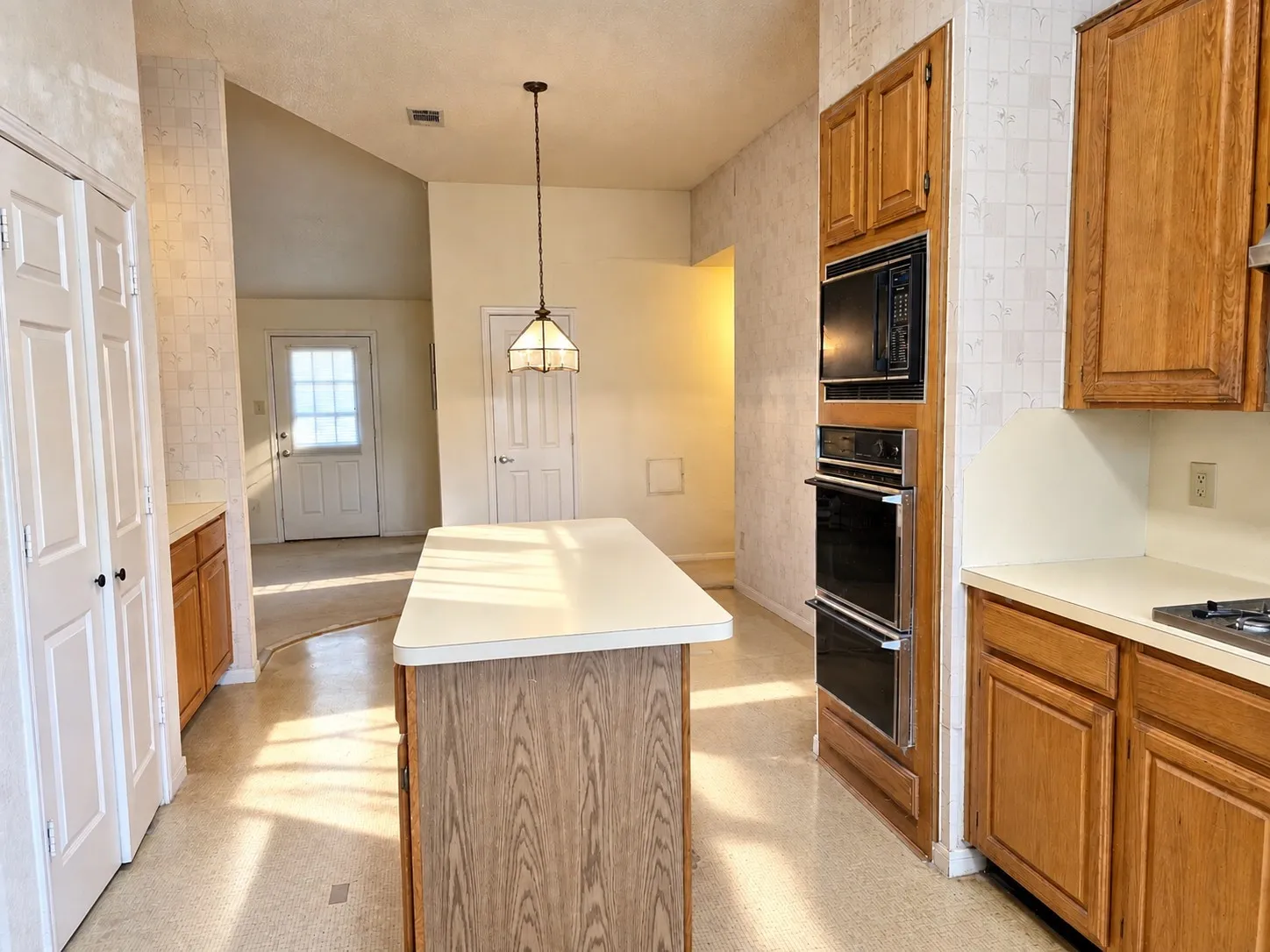 Kitchen featuring a central island with a solid surface countertop, wood-finish cabinetry, built-in double ovens, and a built-in microwave. VIRTUALLY DECLUTTERED USING AI