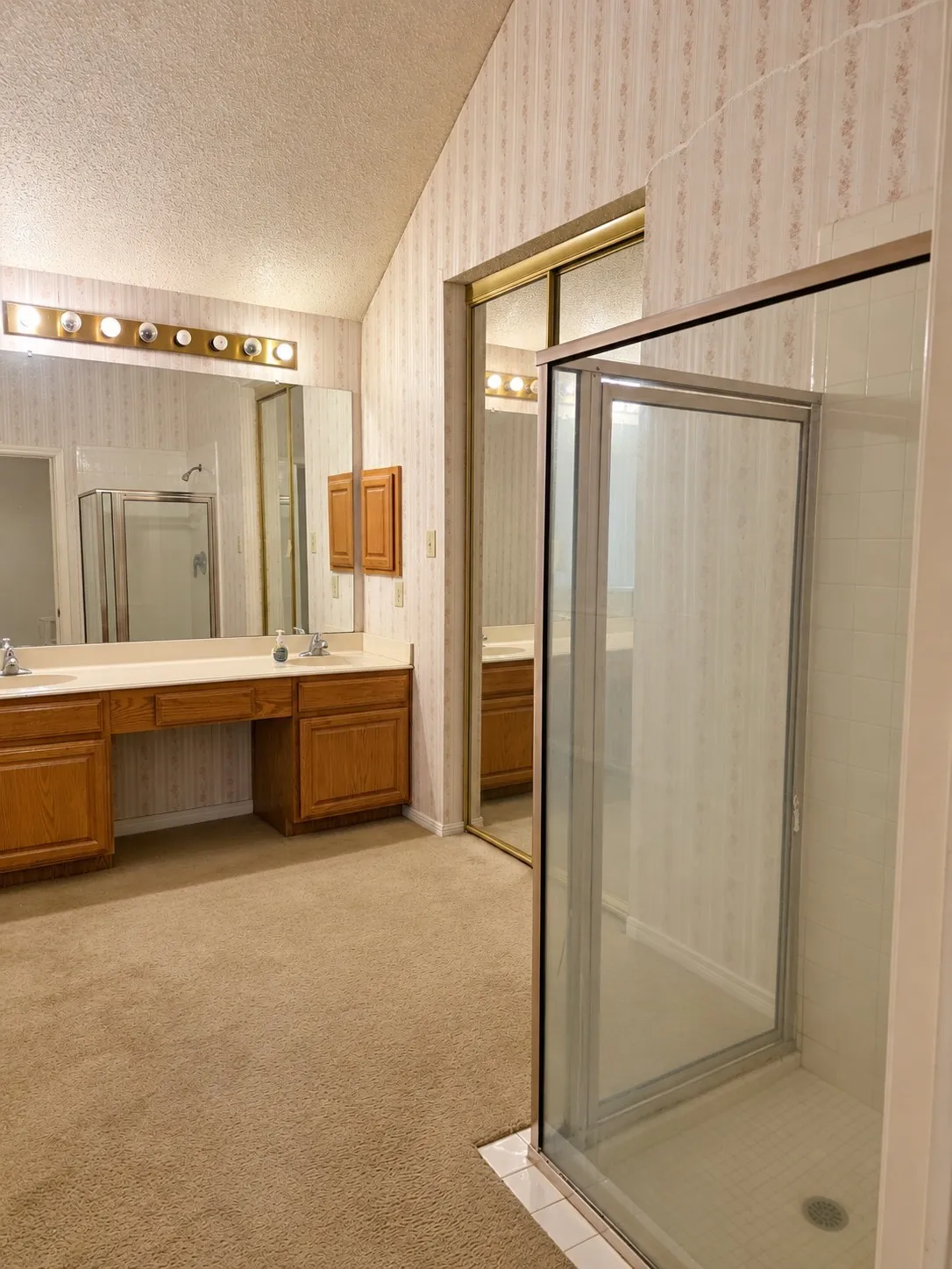 Dual sink vanity with wood-finish cabinetry, illuminated by a multi-bulb fixture. VIRTUALLY DECLUTTERED USING AI