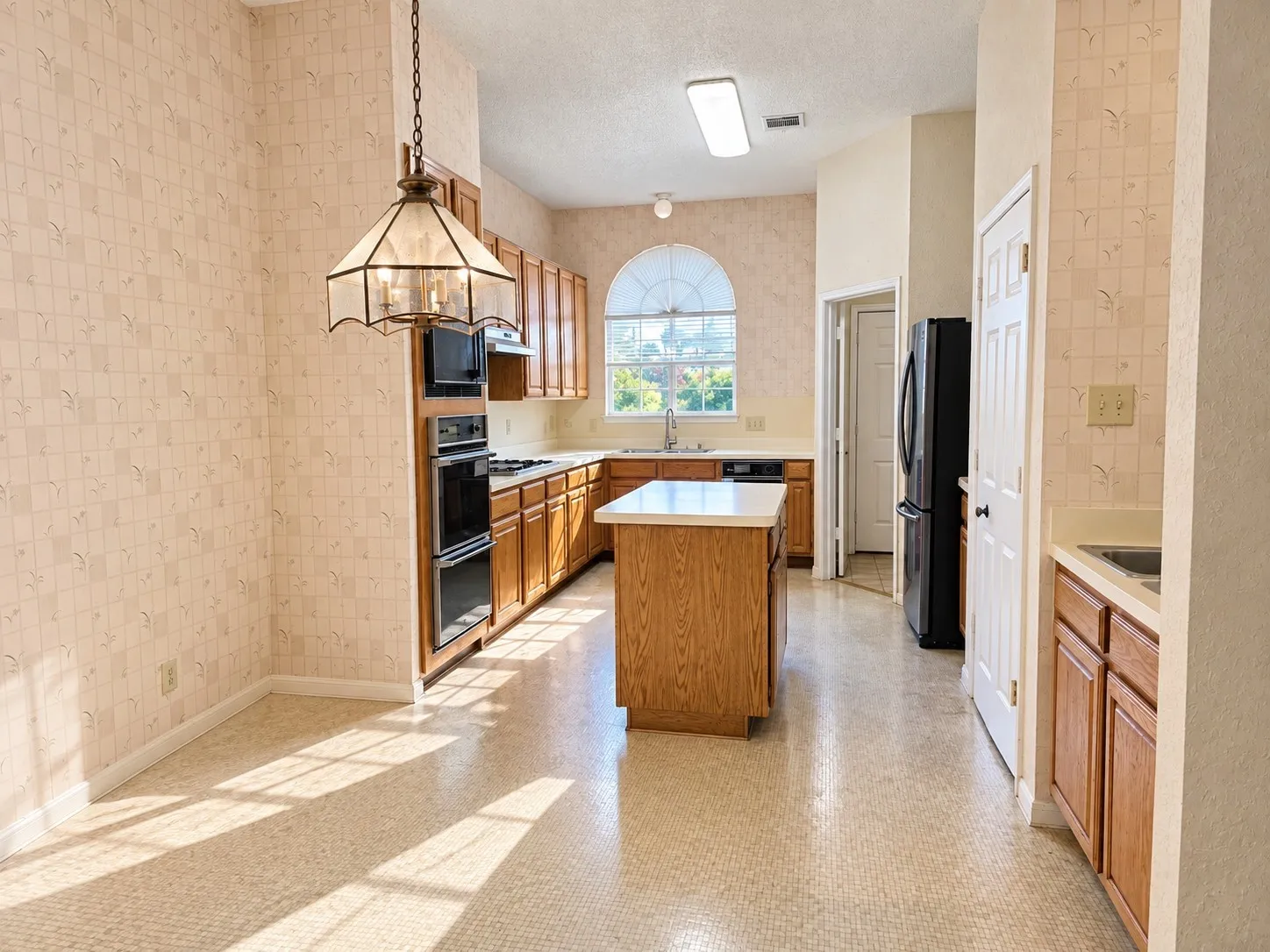 Kitchen with wood cabinetry, a central island, built-in double ovens, and an arched window. VIRTUALLY DECLUTTERED USING AI