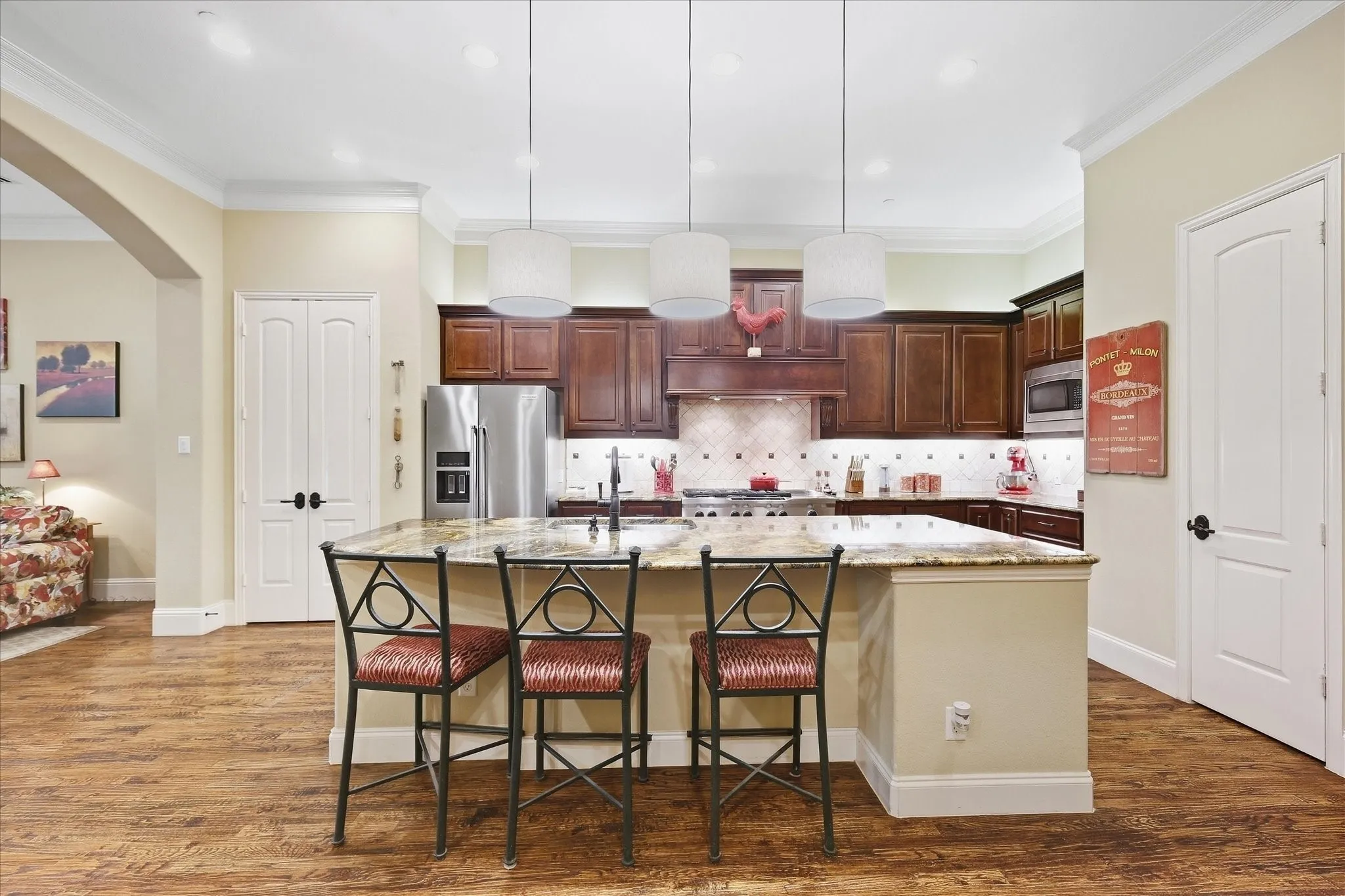 Gourmet kitchen with wood-finish flooring, dark wood cabinetry, an expansive island with a light-colored countertop, stainless steel appliances, and pendant lighting