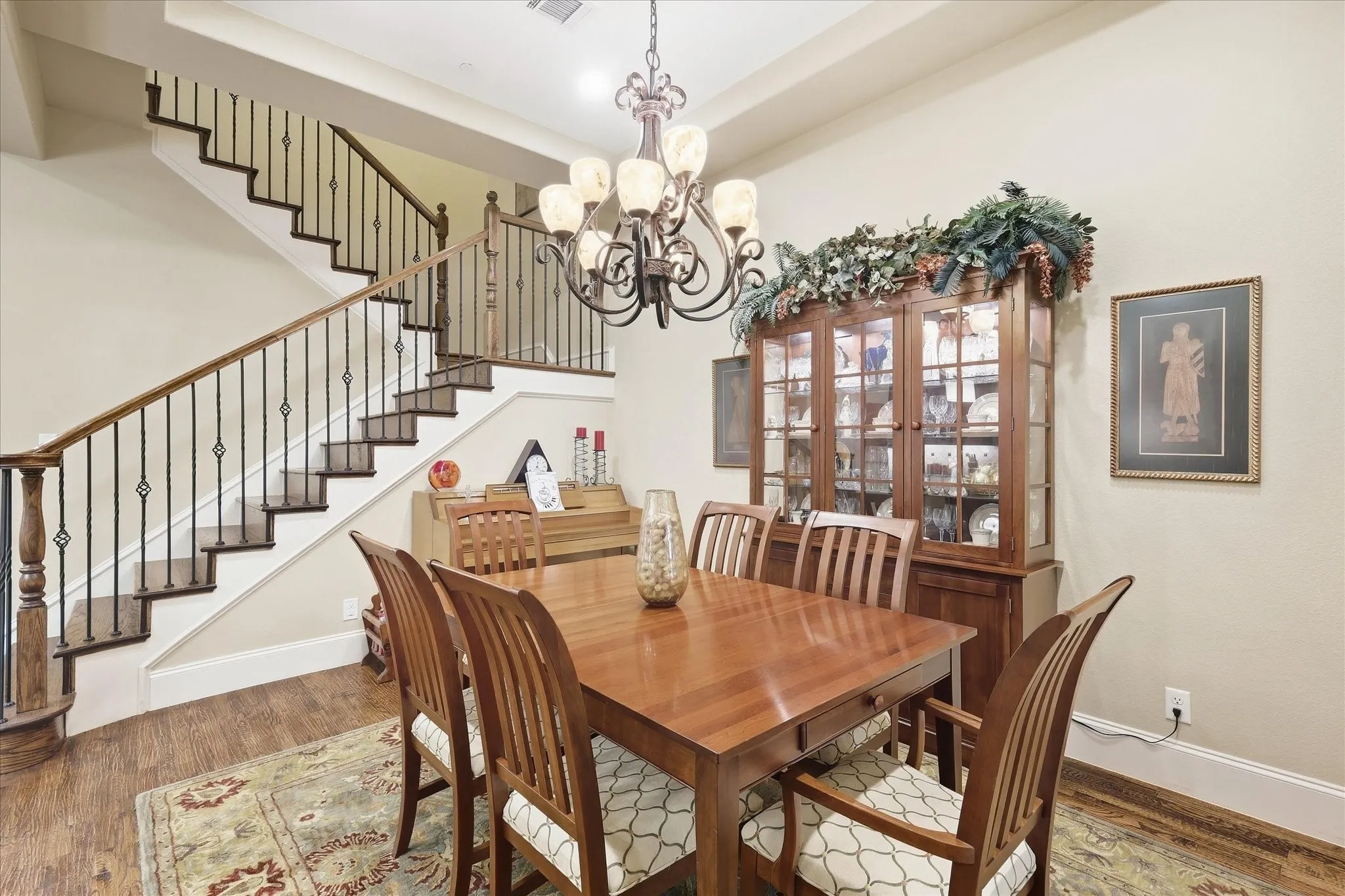Hardwood flooring, staircase with wrought iron balusters and wood handrails, tray ceiling, and a chandelier with glass shades