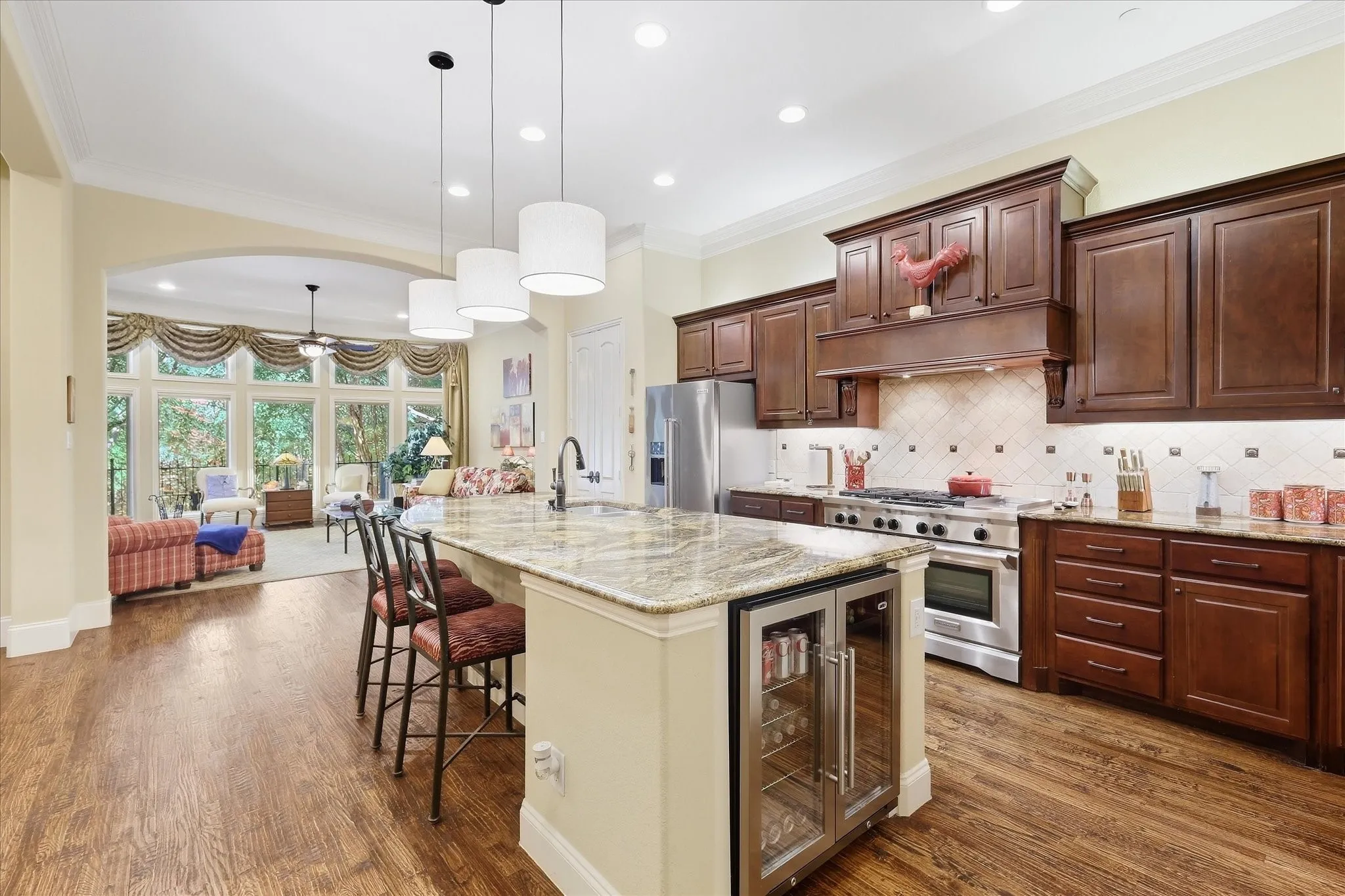 Hardwood flooring throughout, kitchen island with granite countertop, stainless steel appliances, custom dark wood cabinetry, and a beverage refrigerator
