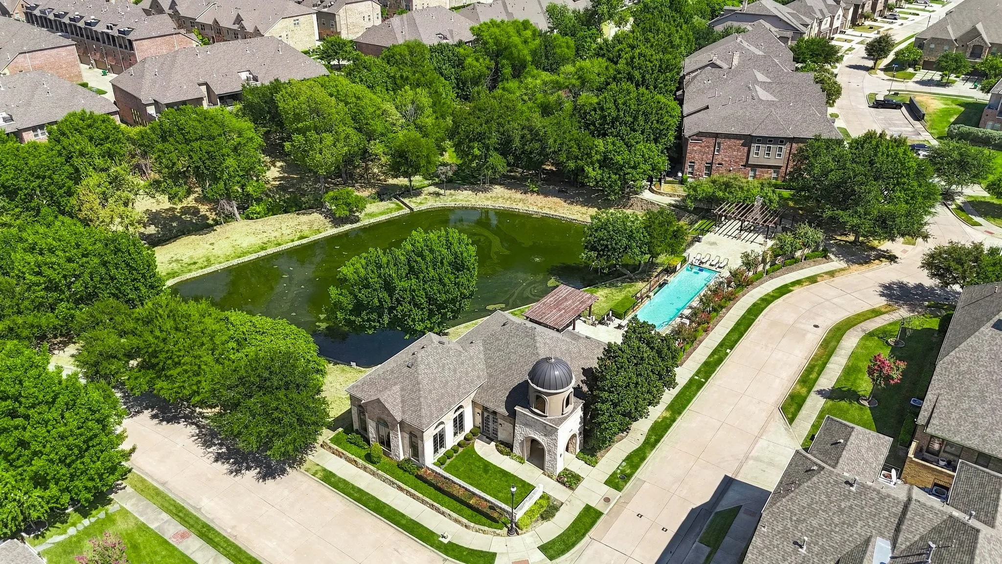 Community pool with adjacent pergola, surrounded by mature trees and a tranquil pond