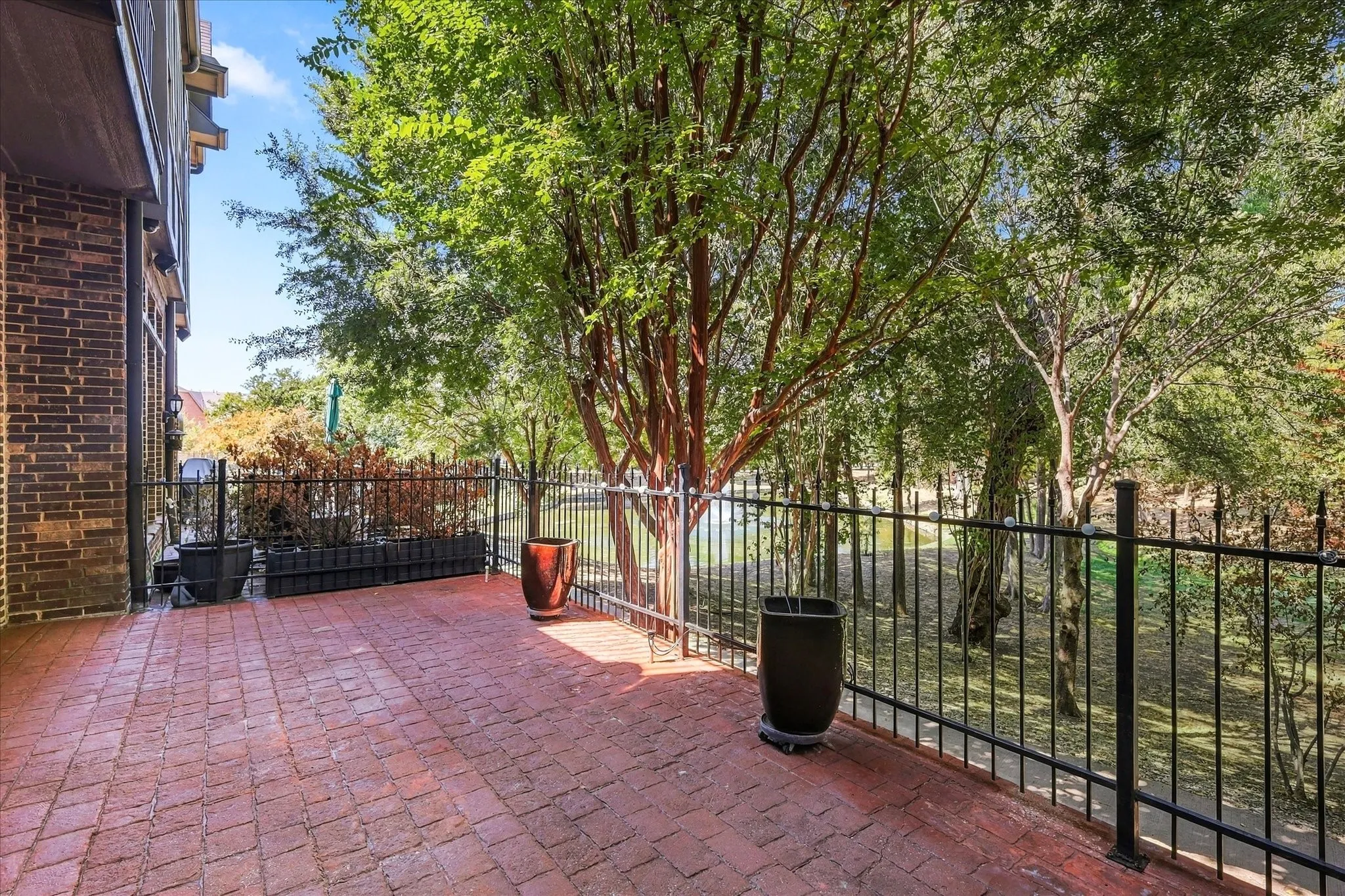 Brick patio with a black metal fence, bordered by mature trees and a brick-clad exterior wall