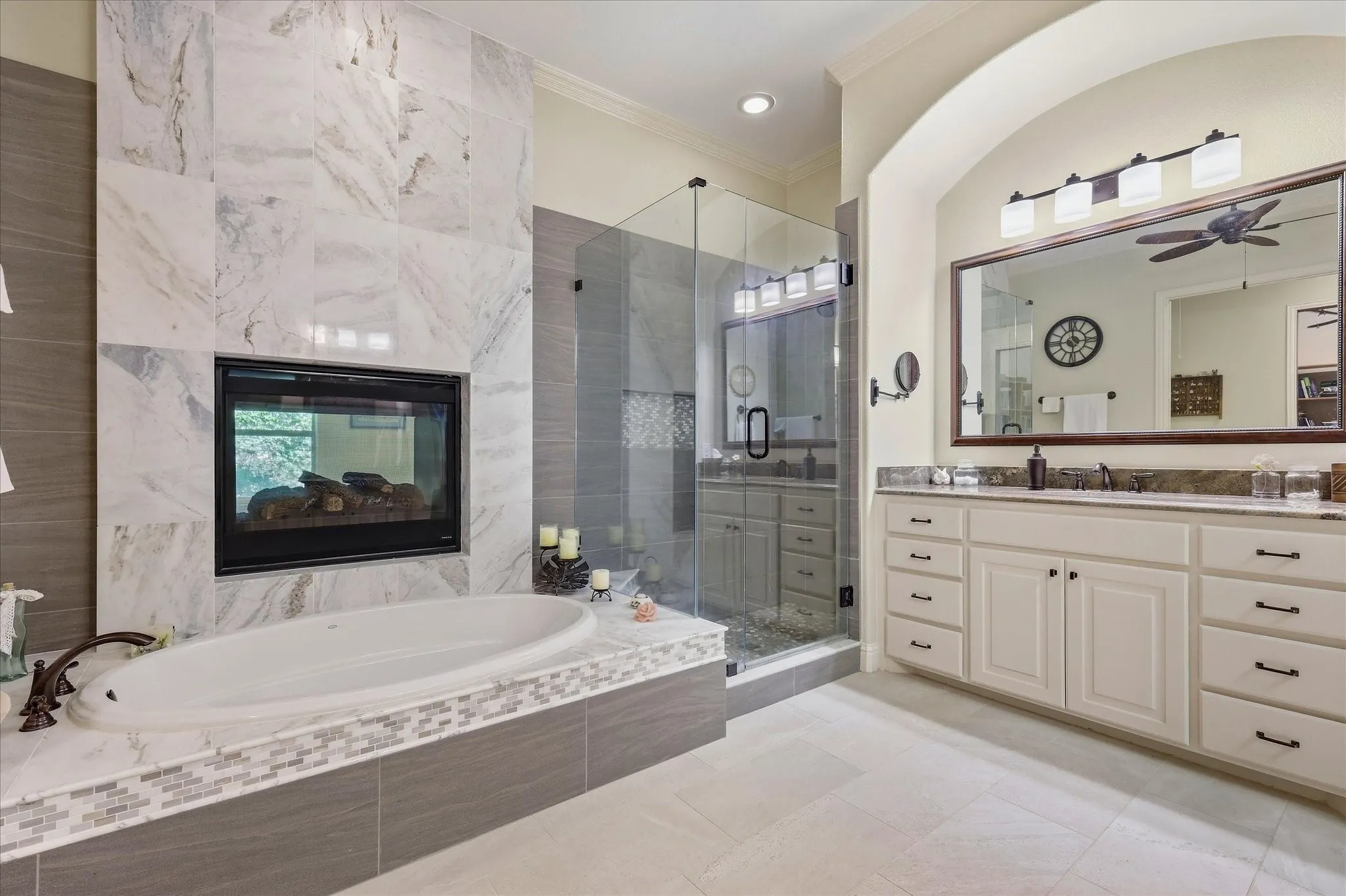 Built-in fireplace, soaking tub with mosaic tile surround, walk-in shower with glass enclosure, dual vanity with undermount sinks, and a large framed mirror