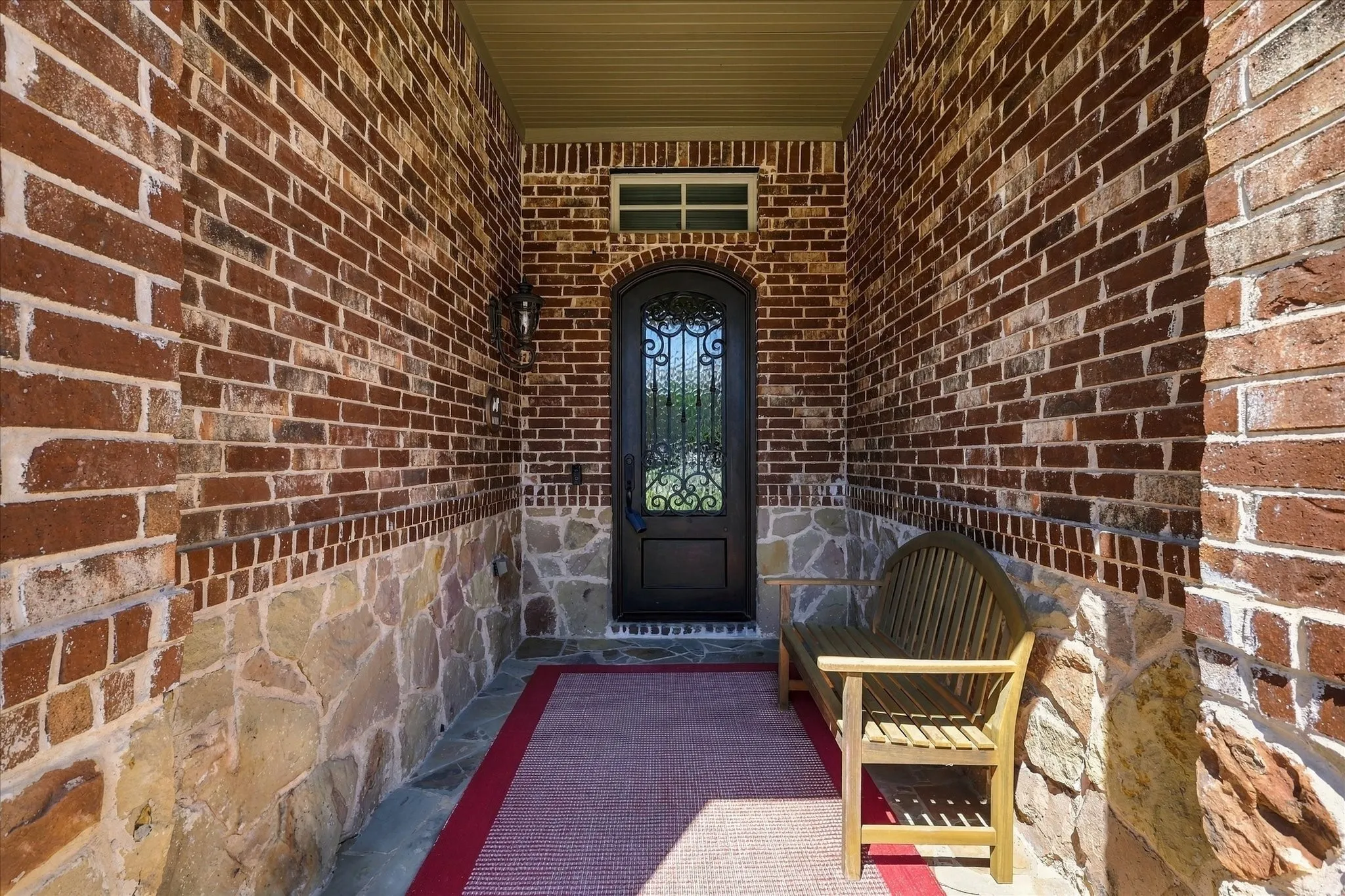 Arched entry door with wrought iron detailing, brick exterior, stone accent wall, flagstone flooring, and recessed lighting