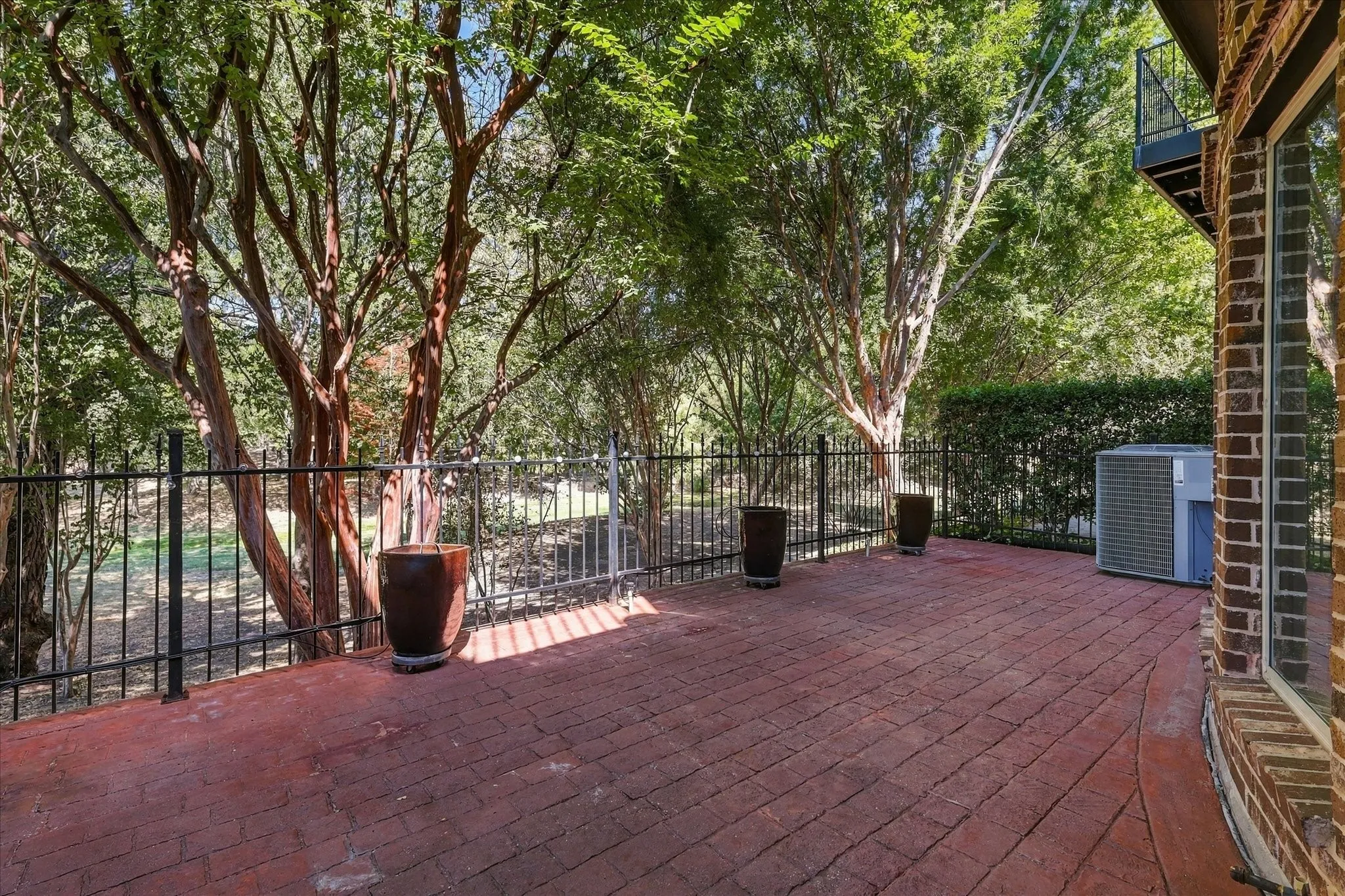Brick patio with a black metal fence, surrounded by mature trees, and an exterior brick wall
