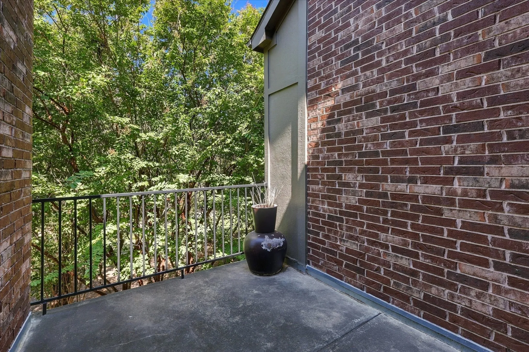 Exterior balcony with a brick wall, concrete flooring, and metal railing
