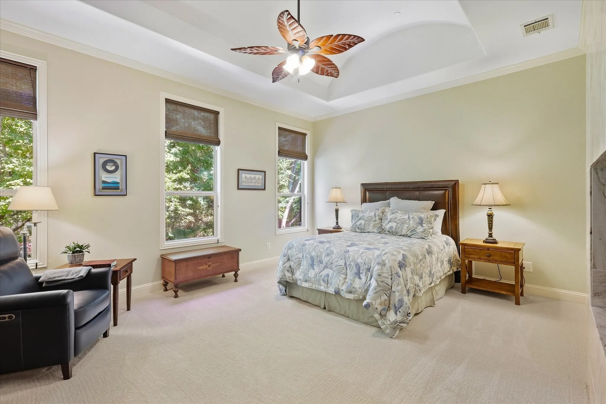 Tray ceiling with a decorative ceiling fan, light-colored carpeting, multiple windows, and a wood-finish bed frame