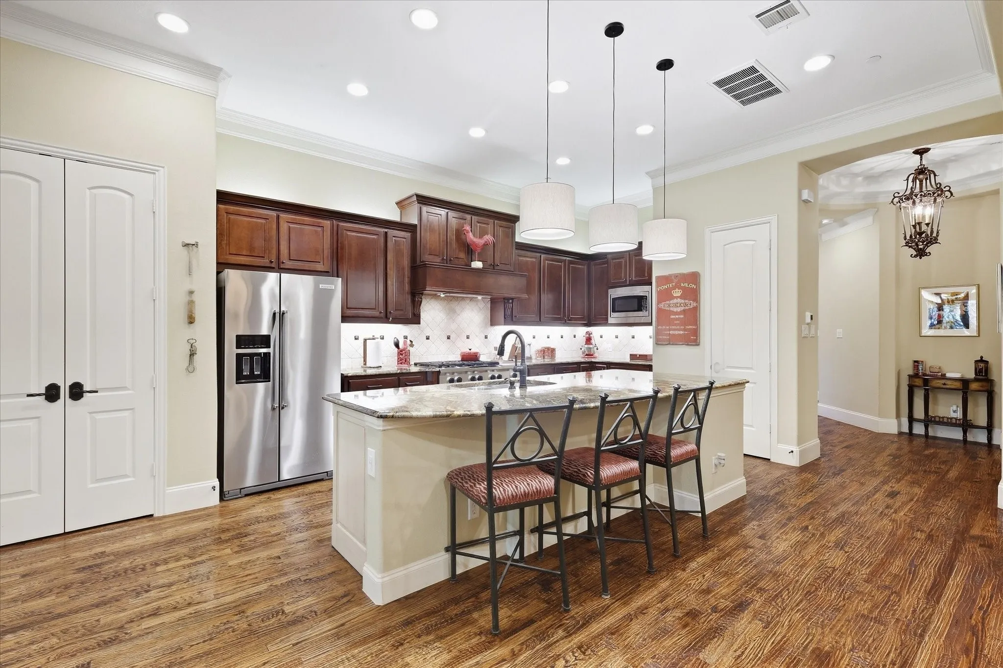 Gourmet kitchen featuring wood-finish flooring, custom wood cabinetry, a central island with countertop seating, recessed lighting, and stainless steel appliances