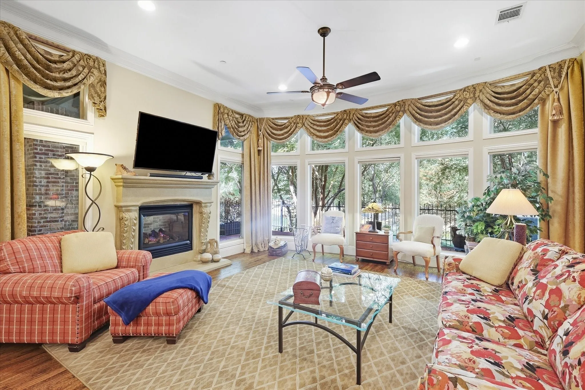 Living area featuring a floor-to-ceiling window wall, a decorative fireplace with a stone-finish mantel, wood-finish flooring, a ceiling fan, and recessed lighting