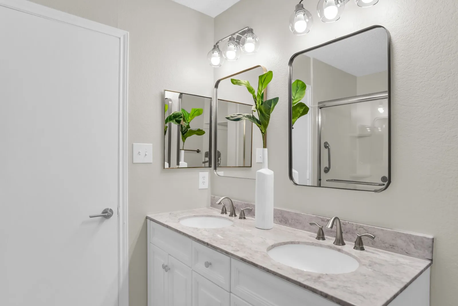 Double vanity with white cabinetry, light-toned countertop, dual undermount sinks, and two framed mirrors illuminated by a multi-bulb fixture