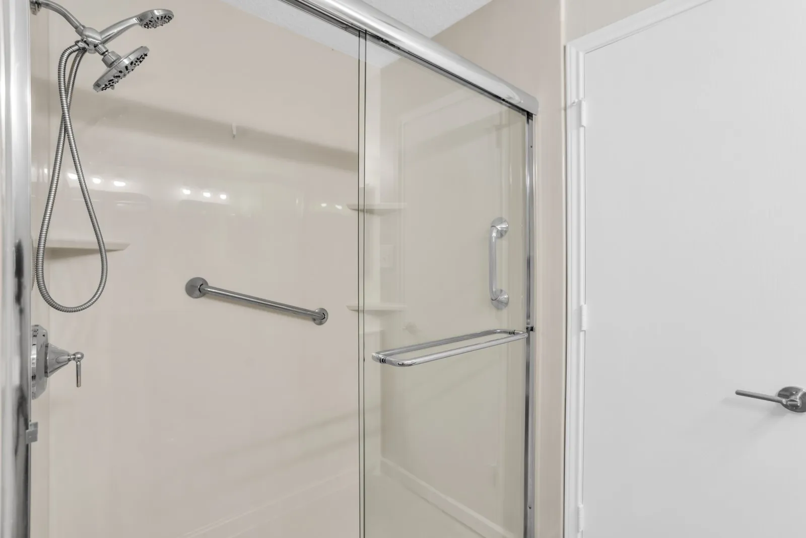 Shower enclosure with clear glass sliding door, dual shower heads, integrated shelving, and support bars
