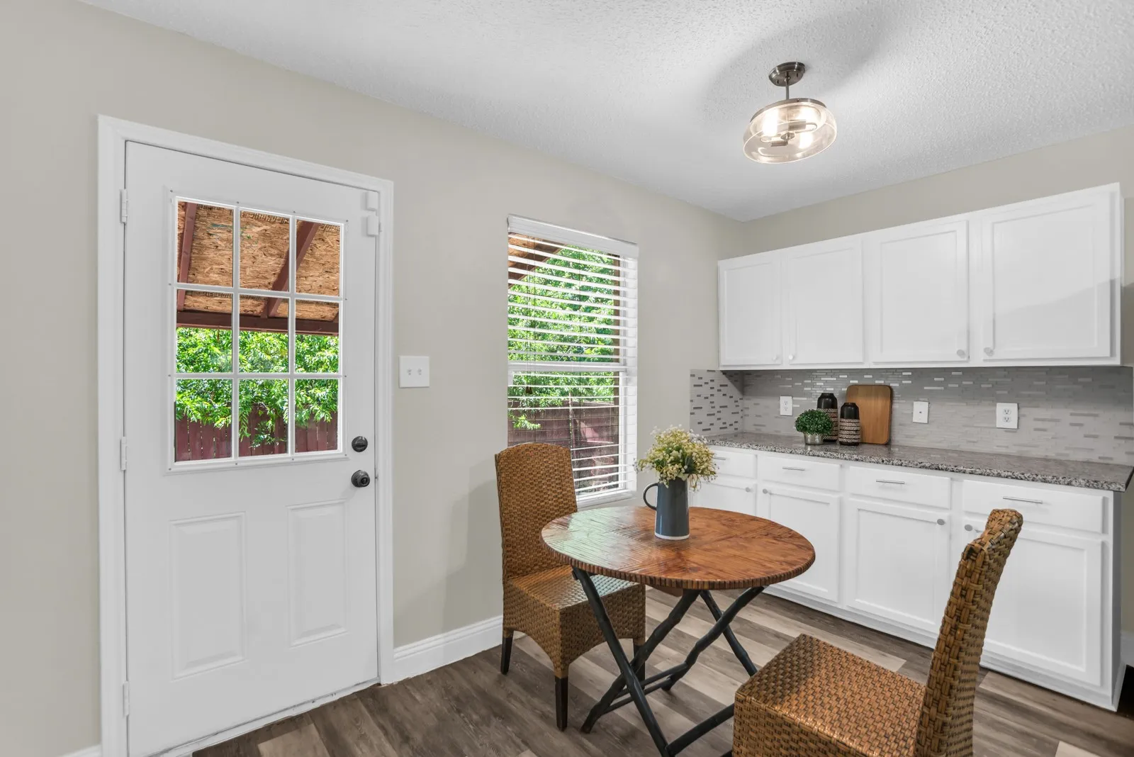 White cabinetry, wood-finish flooring, mosaic tile backsplash, flush-mount ceiling light, and a window with blinds