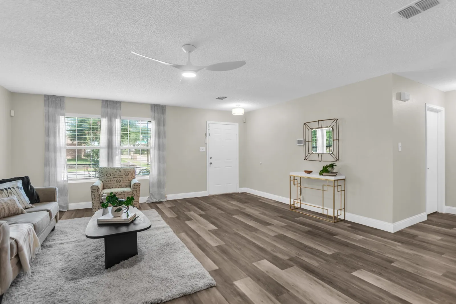 Spacious living area featuring wood-finish flooring, light-colored walls, and a ceiling fan with integrated lighting