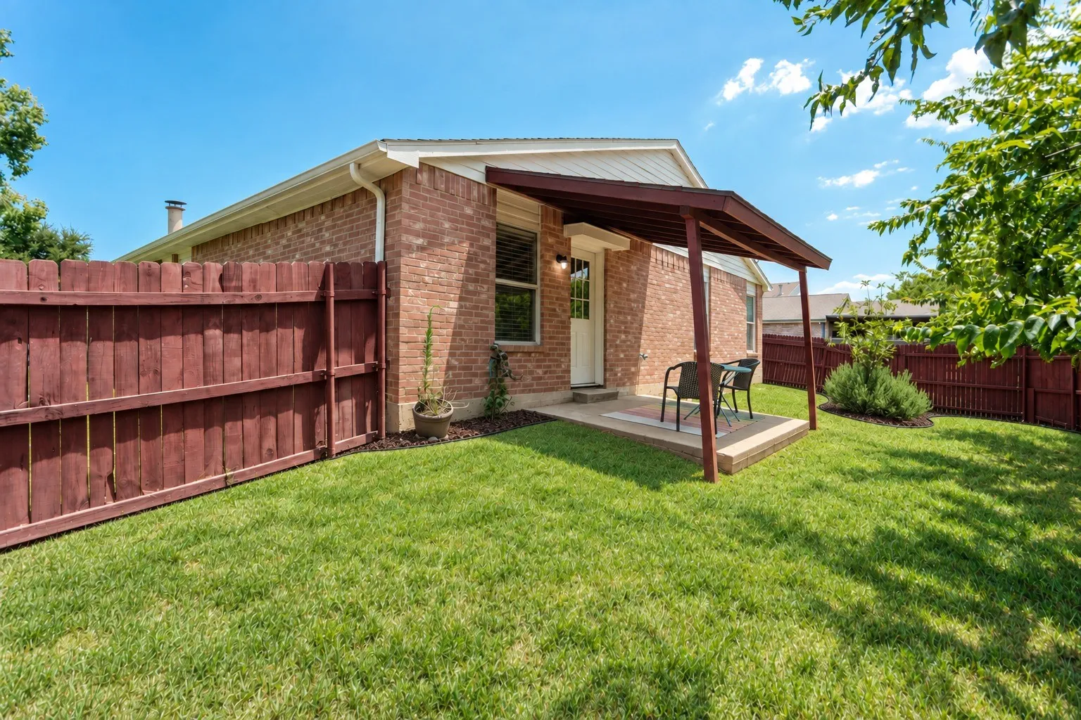 Expansive rear yard featuring a covered patio, brick exterior, and full privacy fencing
