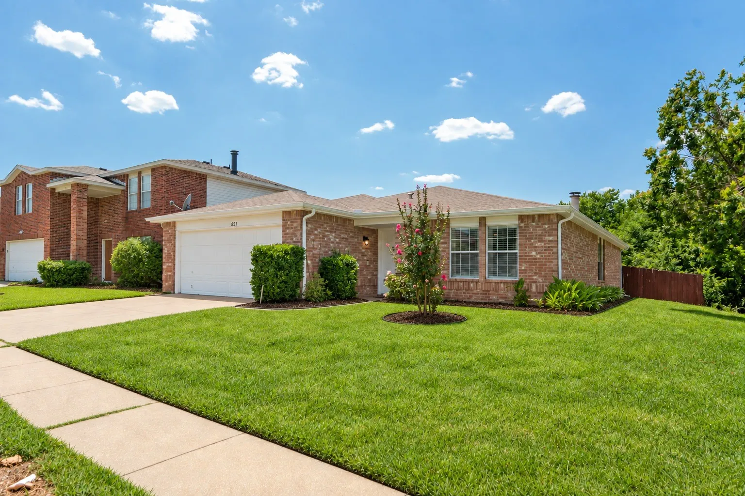 Brick exterior, attached two-car garage, mature landscaping, sidewalk access, and sloped terrain