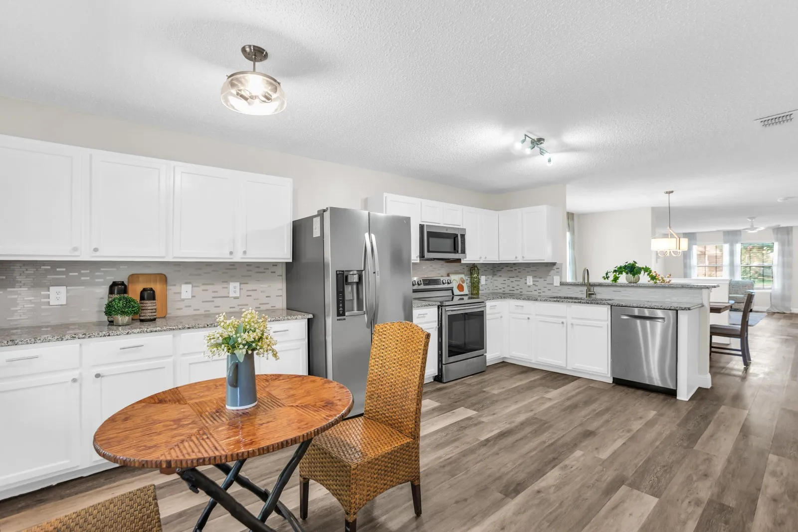 Kitchen featuring white cabinetry, stainless steel appliances, granite countertops, tile backsplash, and wood-finish flooring