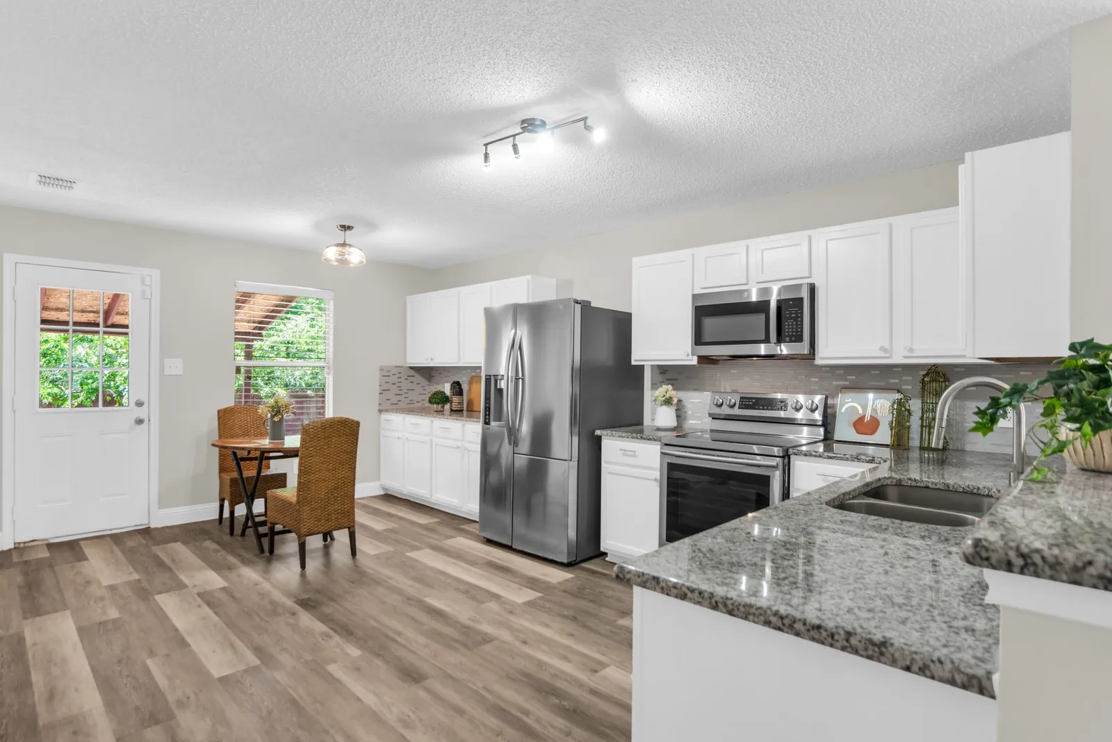 Modern kitchen featuring a stainless steel appliance suite, white cabinetry, granite countertops, and wood-finish flooring