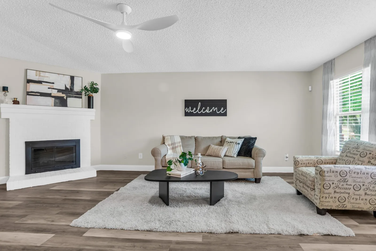 Living space featuring wood-finish flooring, a white-painted fireplace, and a ceiling fan with integrated lighting