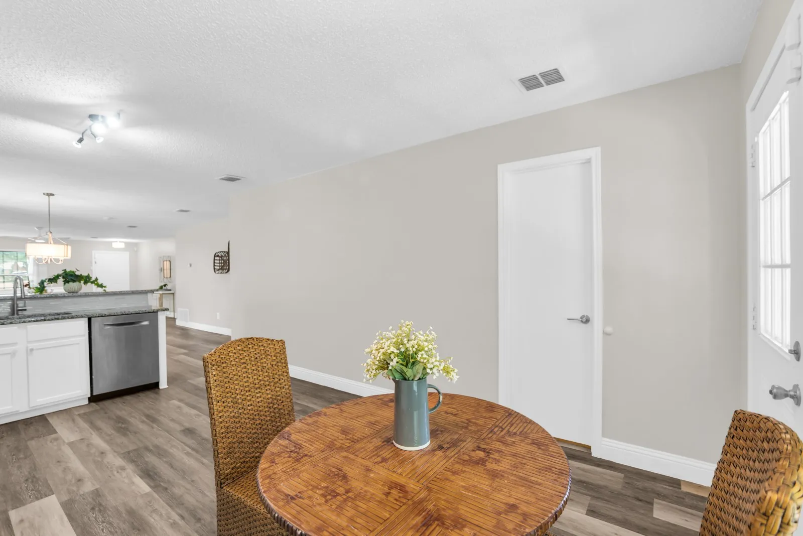 Wood-finish flooring throughout, white interior doors, and a kitchen featuring white cabinetry, a stainless steel dishwasher, and a stone-finish countertop