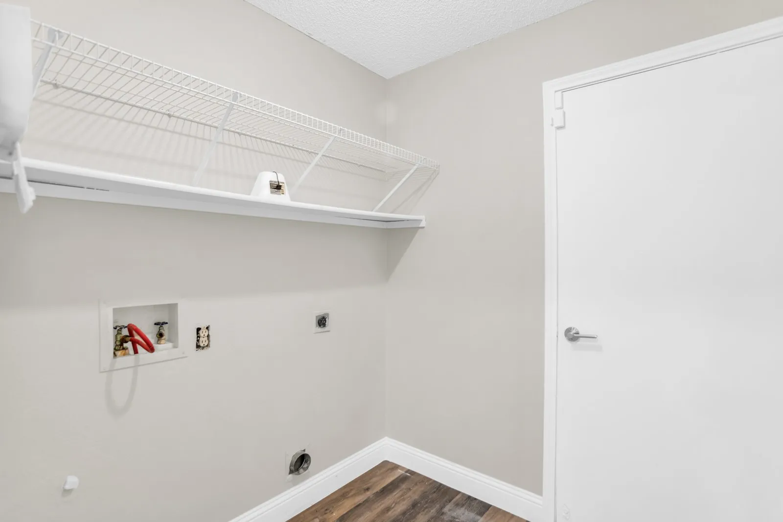 White wire shelving system, wall-mounted laundry hookups, wood-finish flooring, and a flat panel door