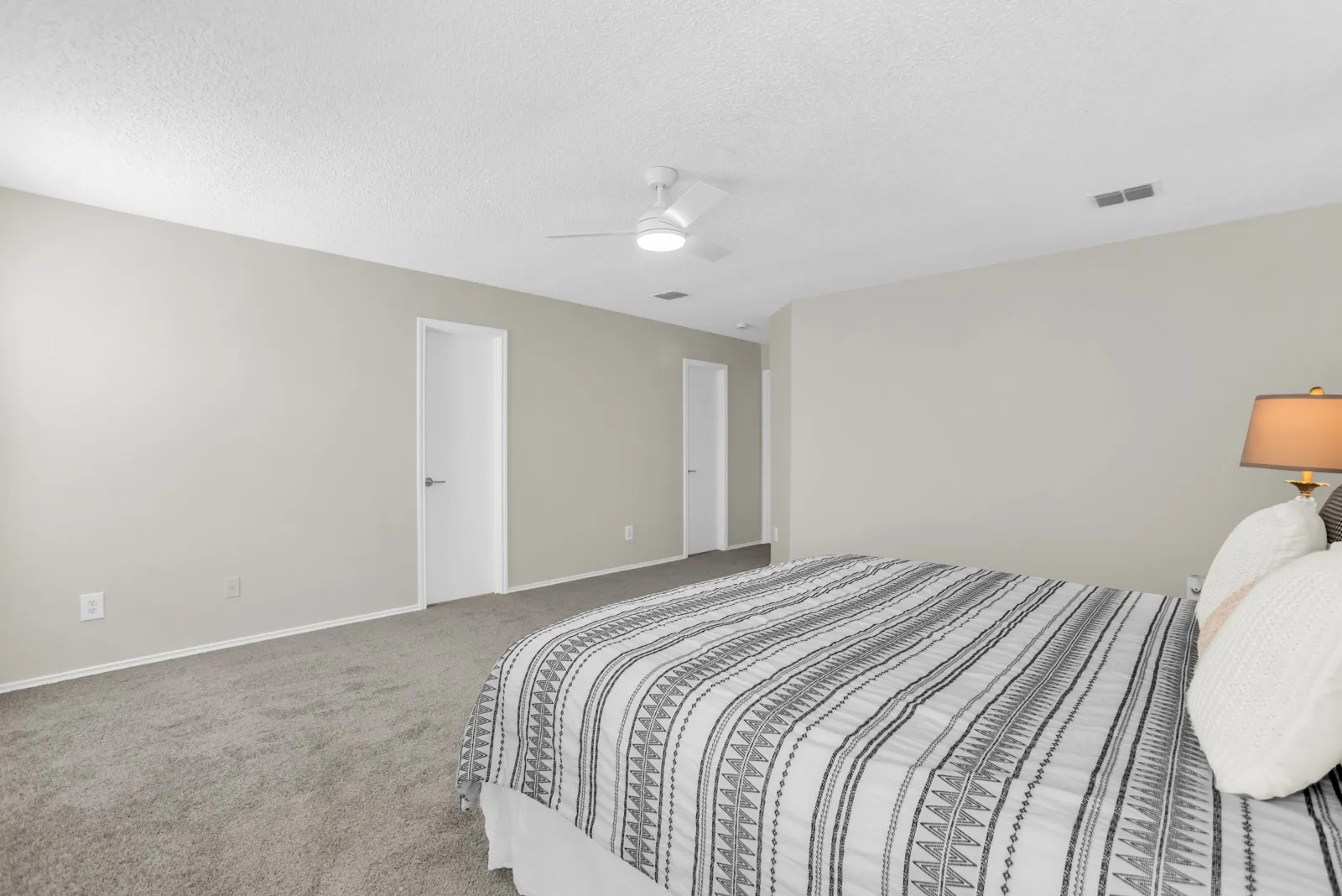 Neutral tone walls, grey carpeting, and a ceiling fan with integrated lighting