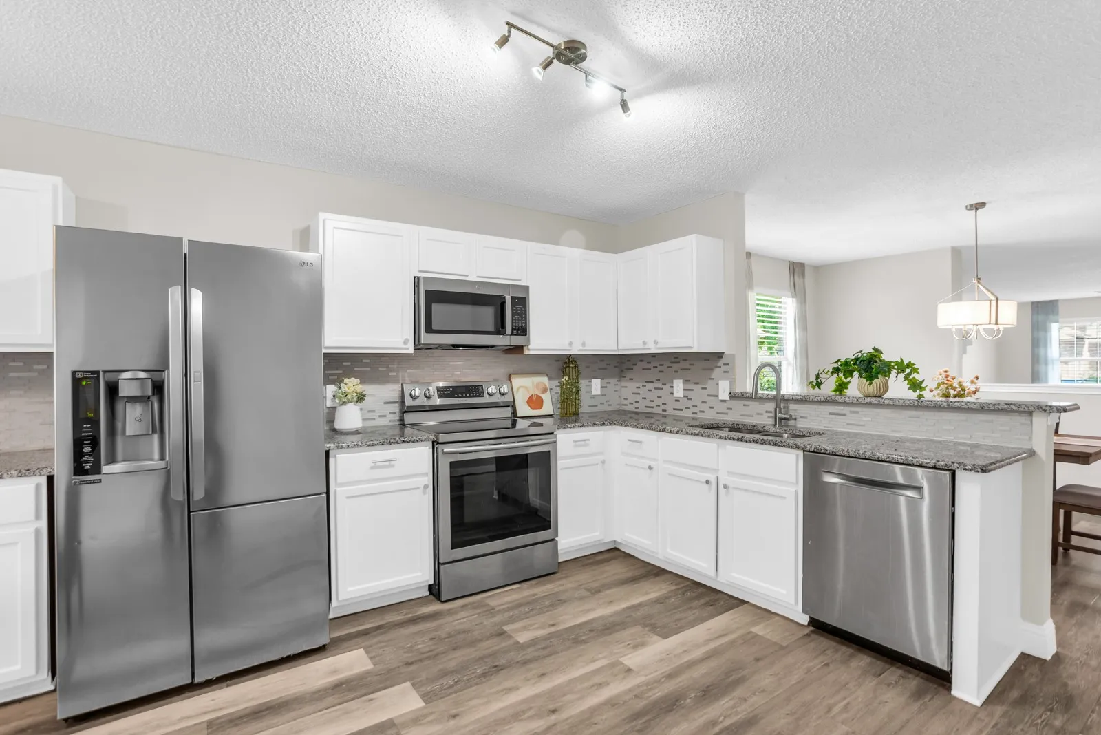 Kitchen featuring stainless steel appliances, wood-finish flooring, white cabinetry, granite countertops, and a tiled backsplash