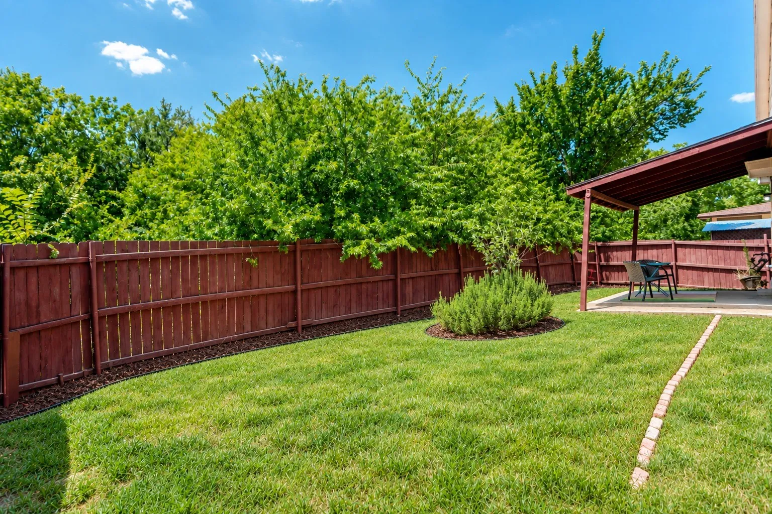 Expansive backyard featuring a manicured lawn, established privacy fence, and a covered patio with a paved surface