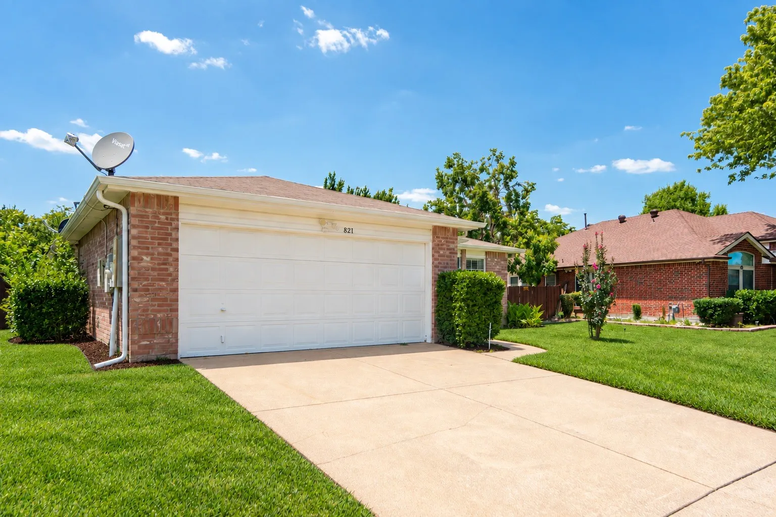 Brick exterior with a white garage door, concrete driveway, and established landscaping
