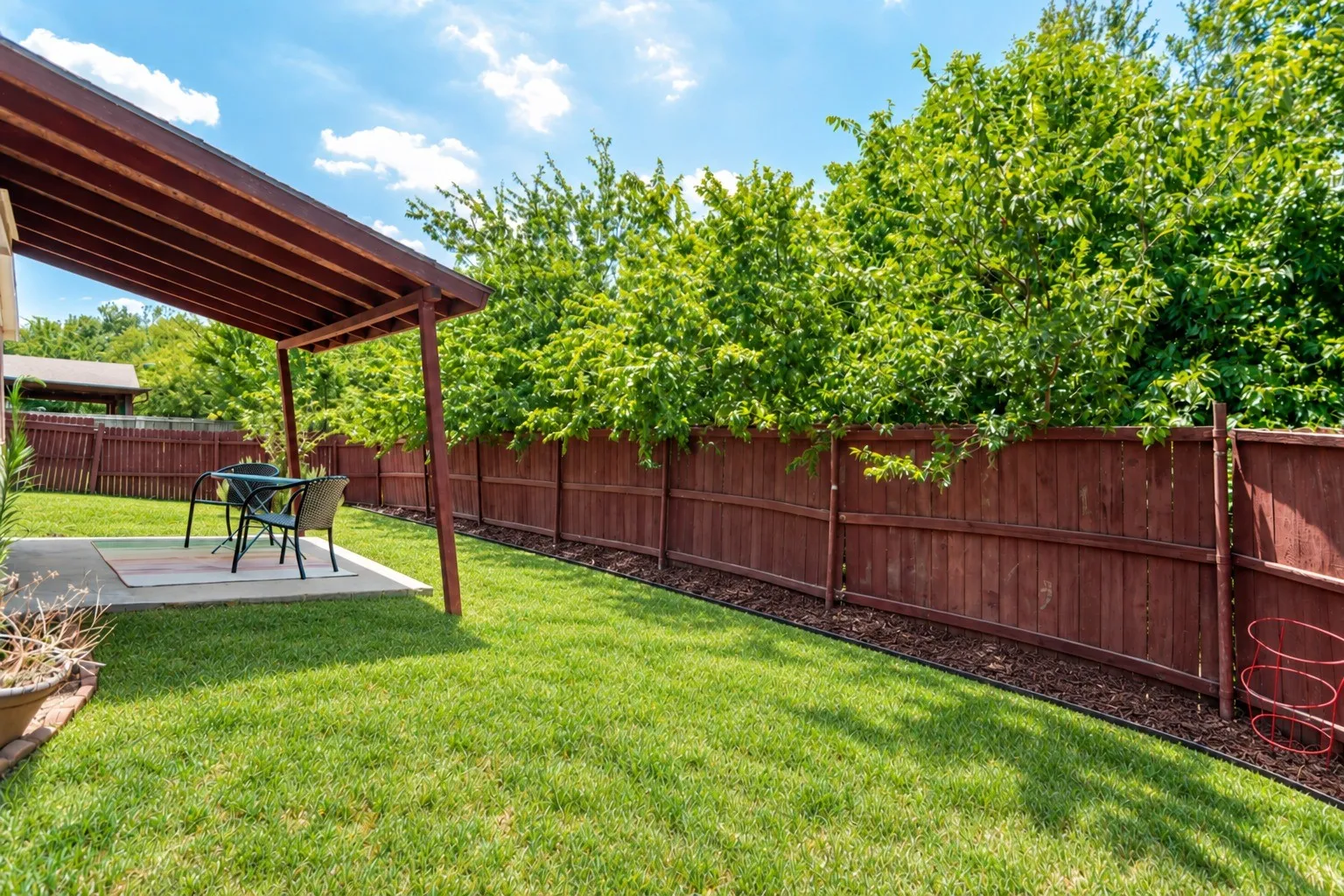 Covered patio with concrete slab, wood-stained fencing, and a manicured lawn