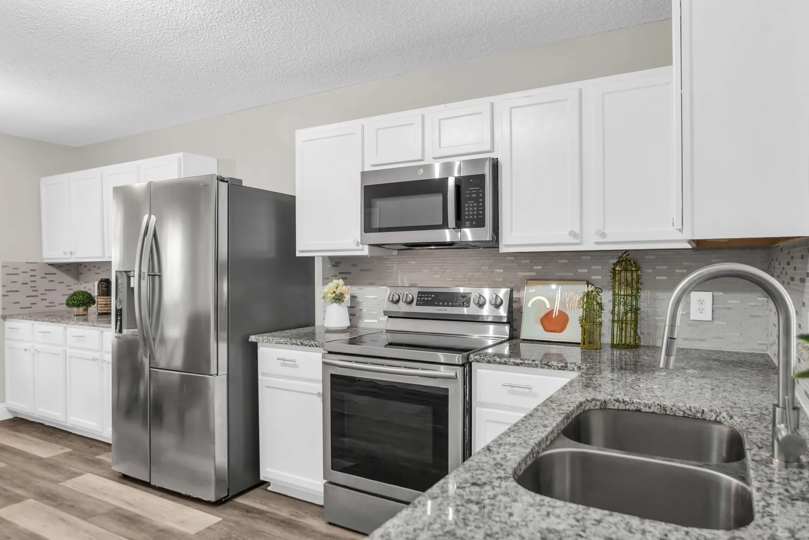 Kitchen featuring stainless steel appliances, white cabinetry, a dual basin sink, granite countertops, and a tile backsplash