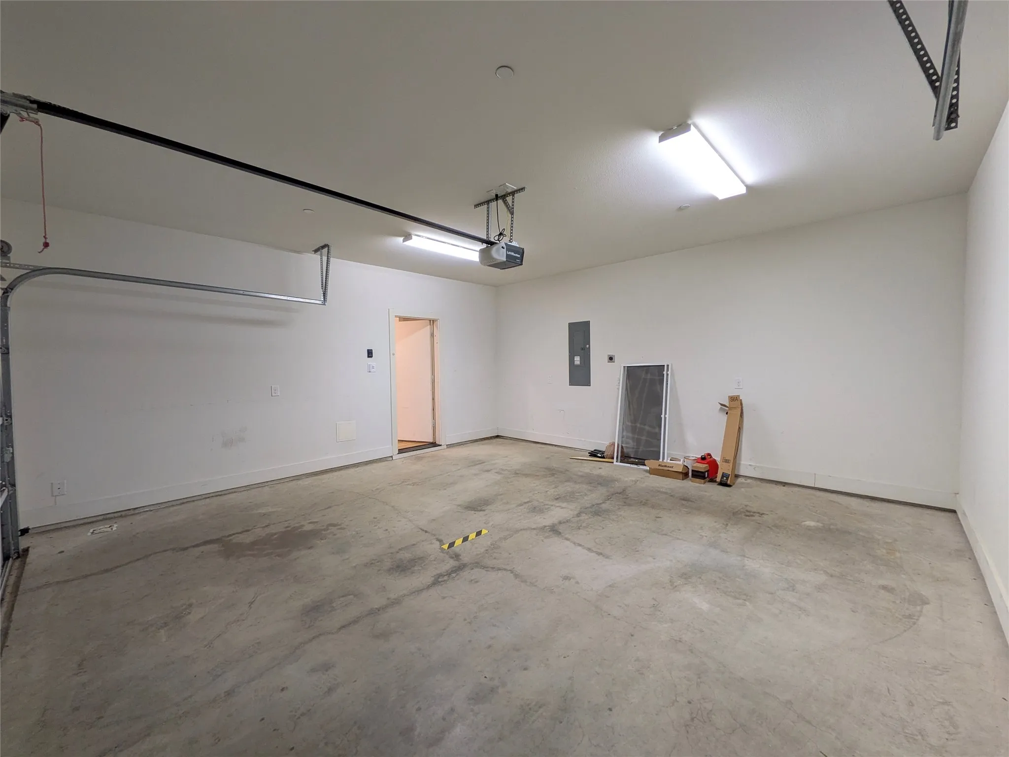 Spacious garage featuring concrete flooring, an automatic garage door opener, and wall-mounted lighting
