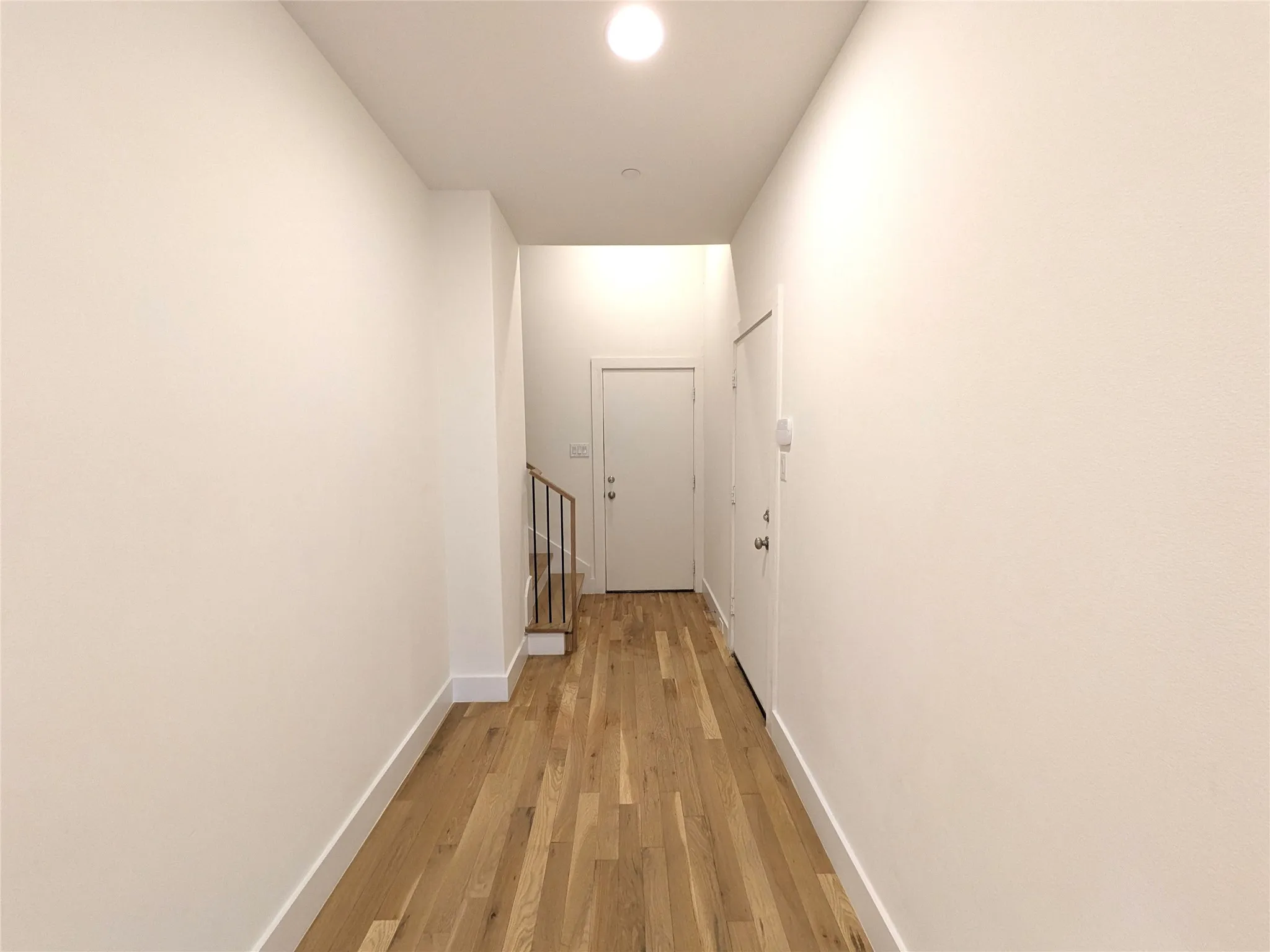 Hardwood flooring, recessed ceiling light, white interior doors, and staircase with metal railing