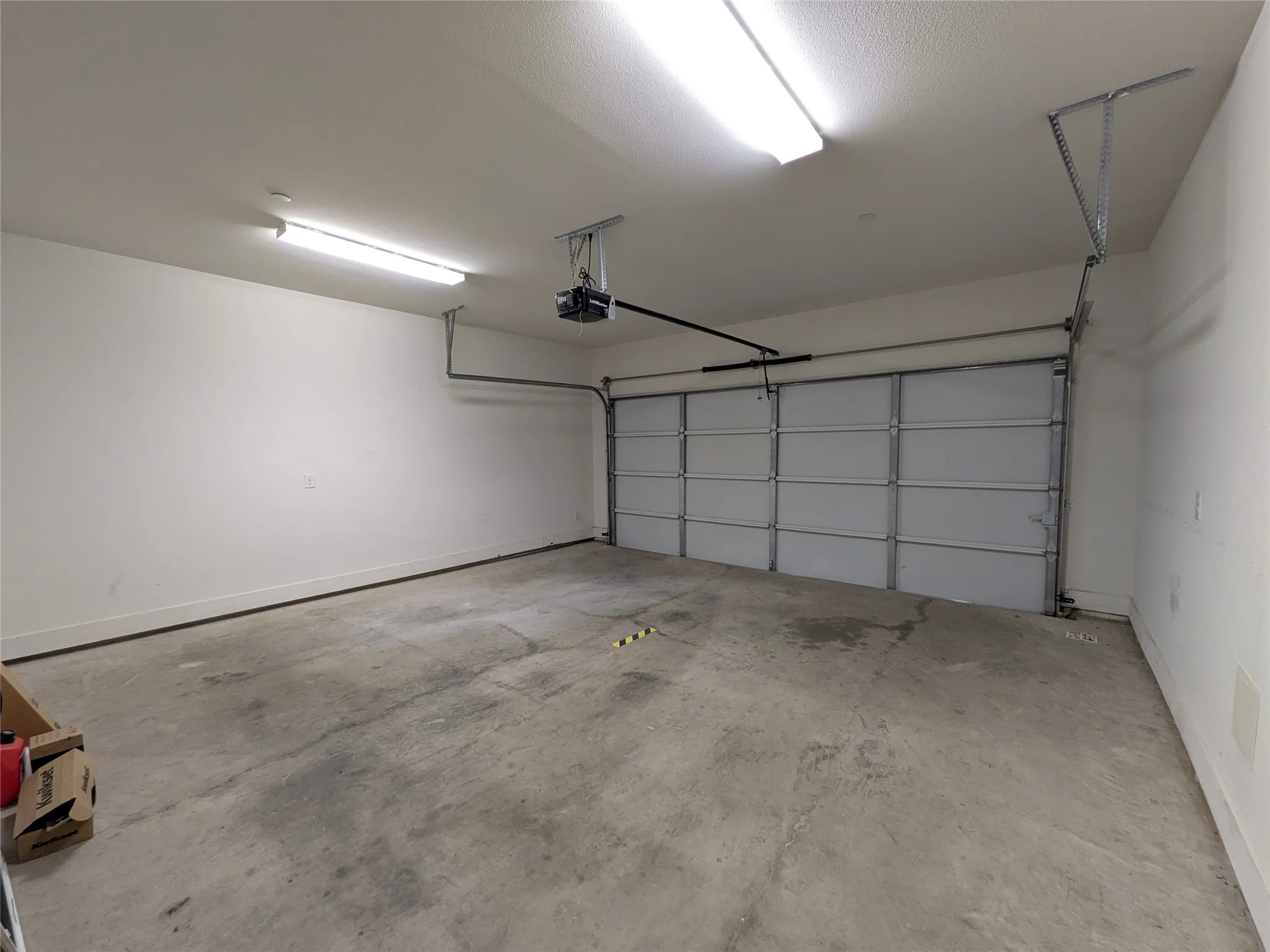 Spacious garage with concrete flooring, automatic garage door, and overhead fluorescent lighting