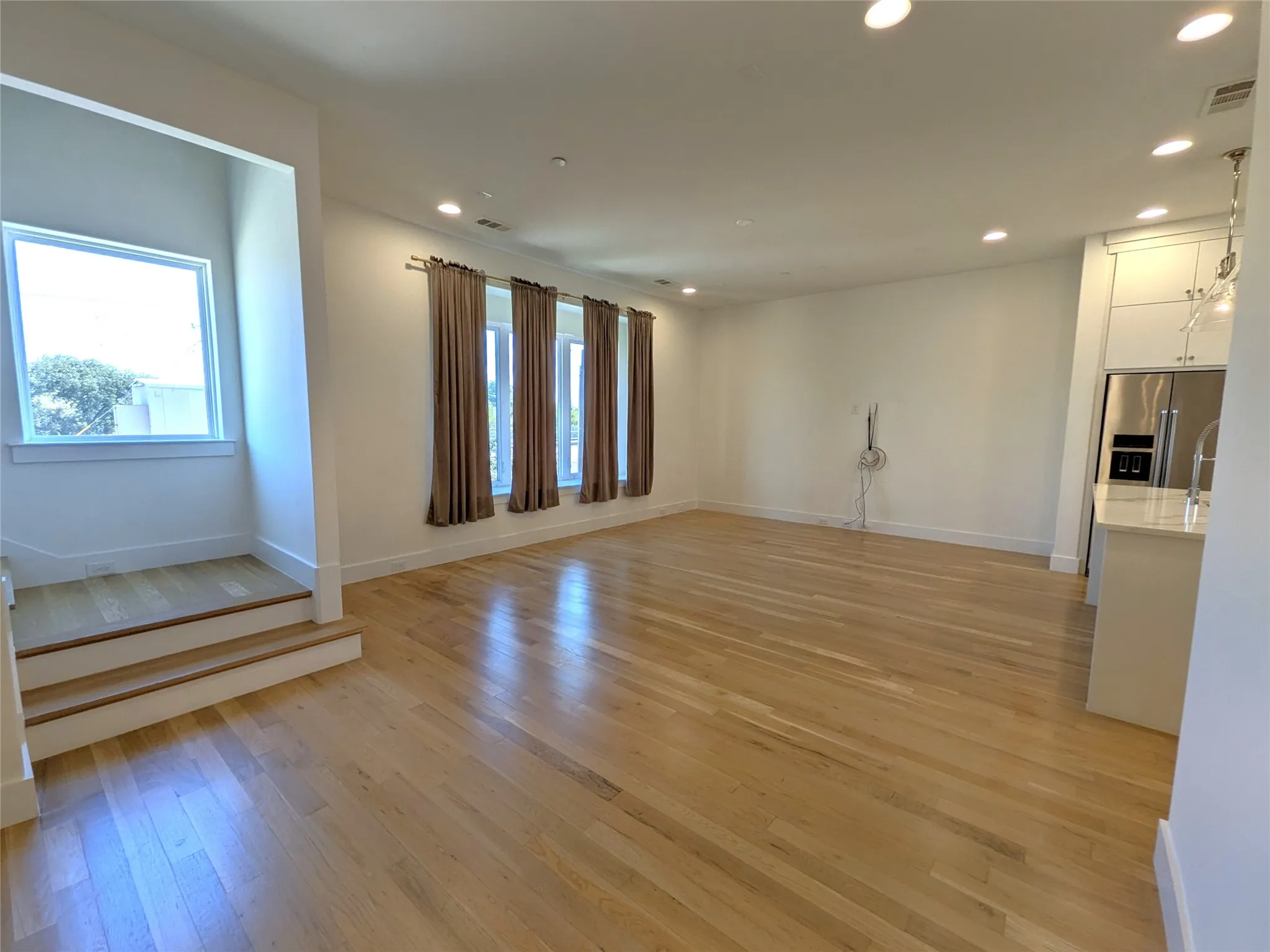 Hardwood flooring throughout, recessed lighting, multiple windows, built-in kitchen cabinetry, and stainless steel refrigerator