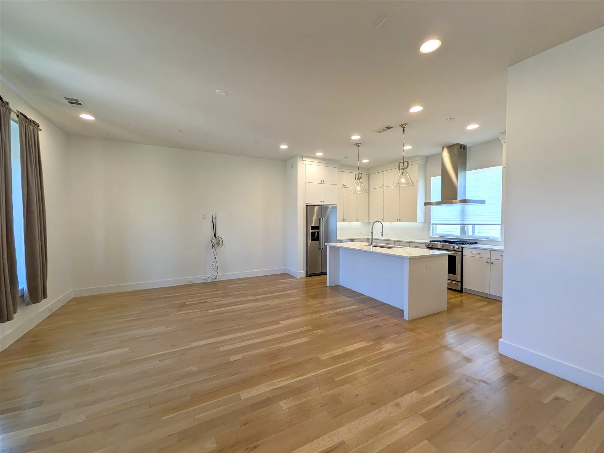 Open-concept living space featuring wood-finish flooring, recessed lighting, a kitchen island with seating, stainless steel appliances, and pendant lighting
