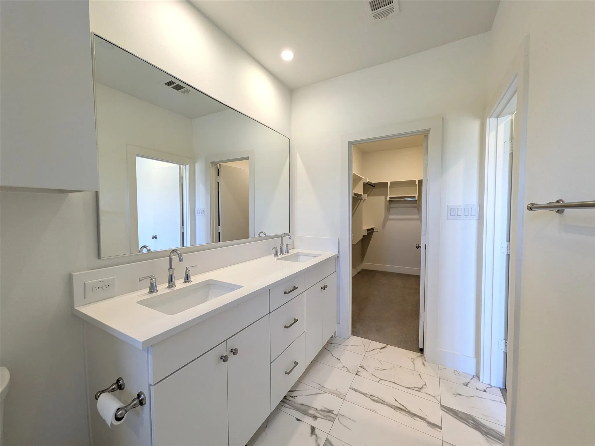 Dual vanity with white cabinetry, polished chrome fixtures, and a large integrated mirror