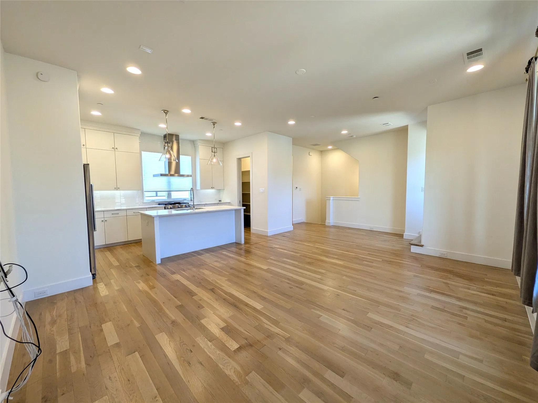 Open-concept living space featuring wood-finish flooring, recessed lighting, and a kitchen with white cabinetry, a center island, and stainless steel appliances